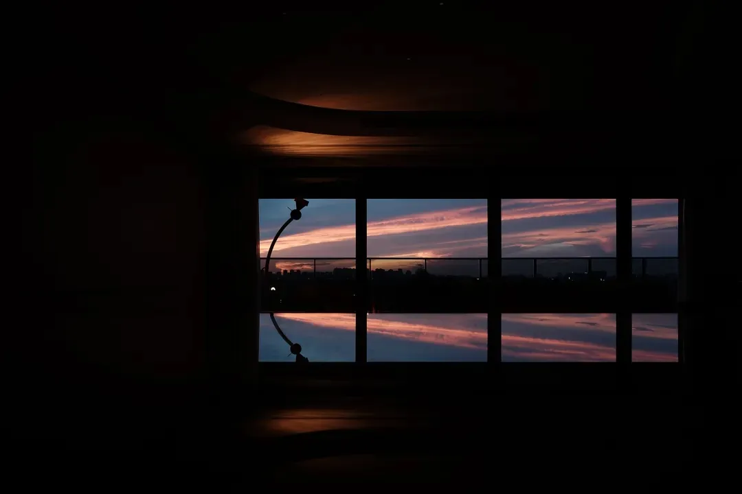 Dimly lit interior space with a large window reflecting the sky, creating a sense of depth