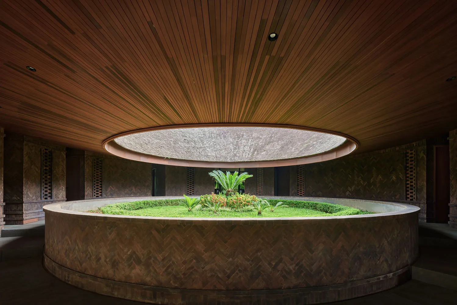 A well-designed interior space with a circular area surrounded by wooden walls, featuring potted plants and a central green plant