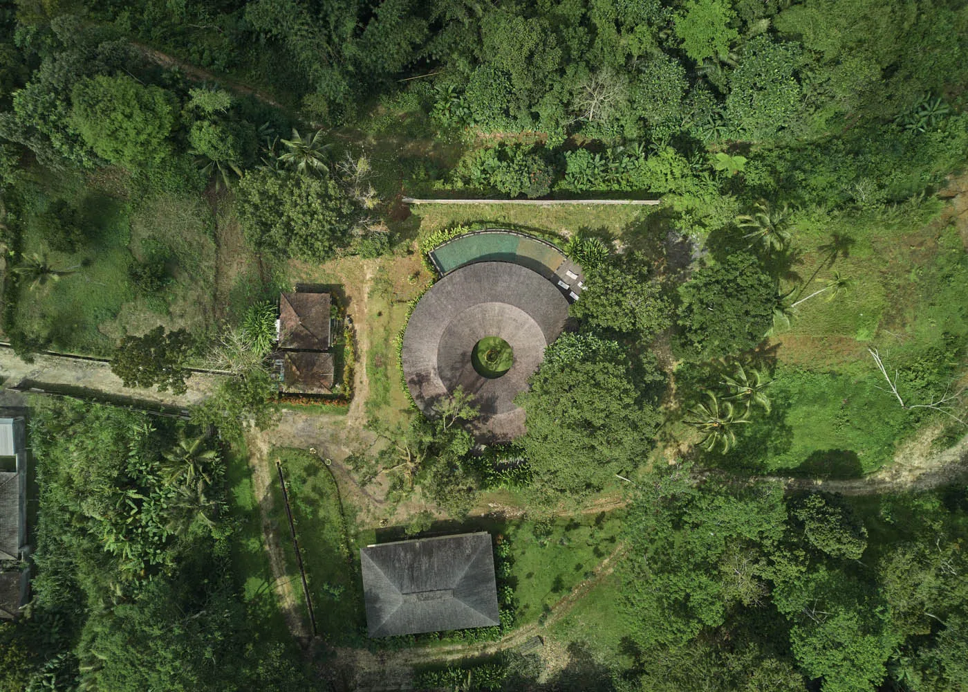 A serene photo of a circular building surrounded by trees in a forest, with a central gathering point and lush greenery