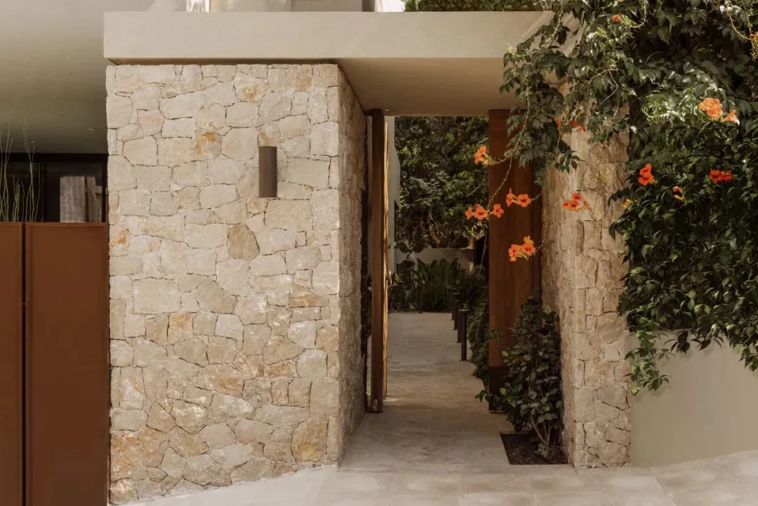 A serene entrance to a house with a brick wall, a doorway, and potted plants, set against a neutral background