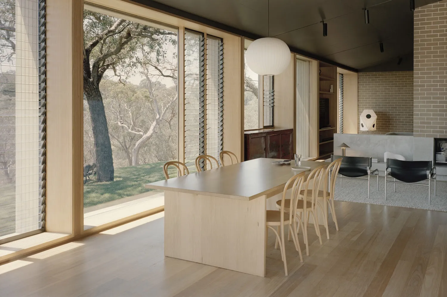 Open living space with a wooden dining table, chairs, and a kitchen area, filled with natural light from windows