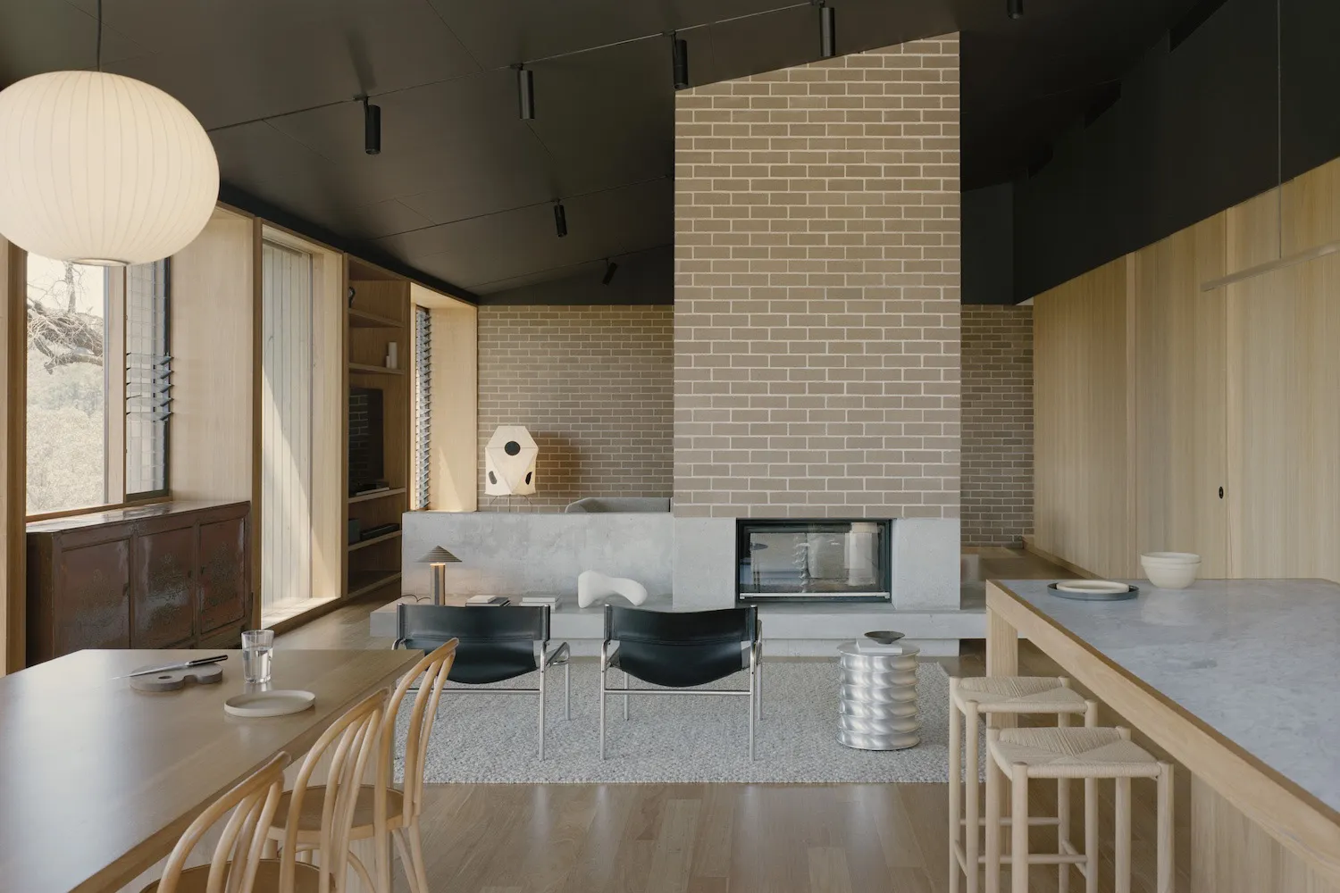 Open modern living area with a brick fireplace, wood paneling walls, and dim lighting, featuring a couch, chairs, and a dining table