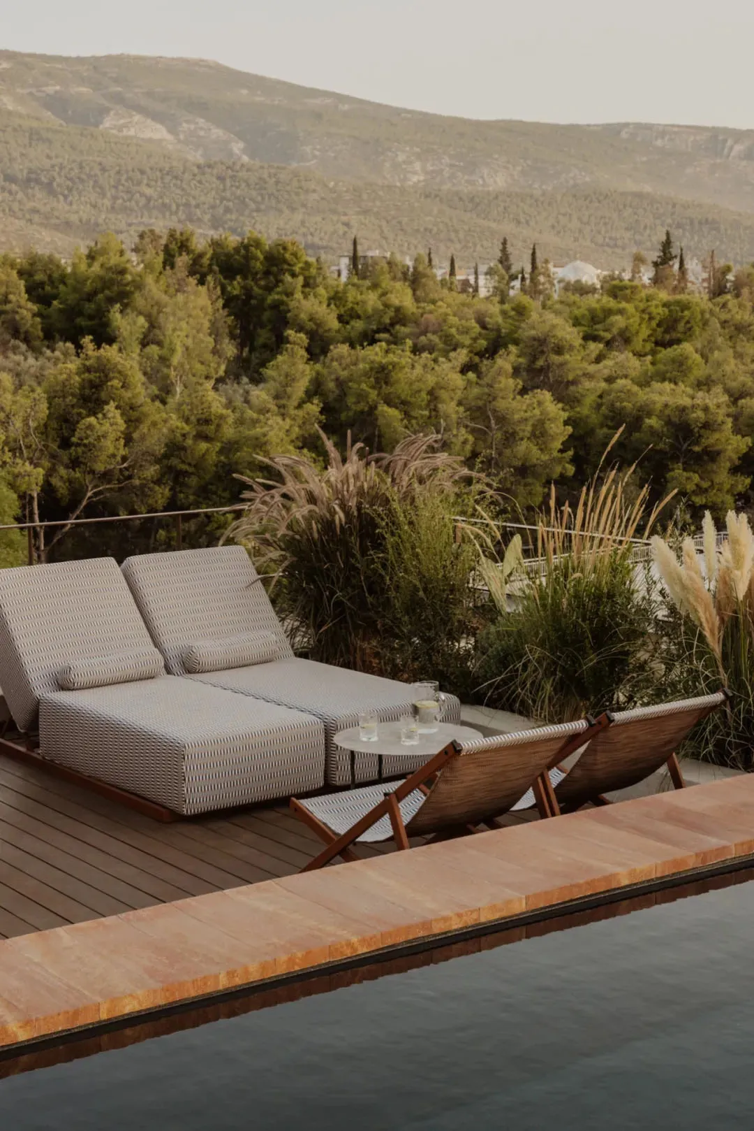 A well-lit outdoor patio area with lounge chairs and couches on a wooden deck near a pool, perfect for relaxation