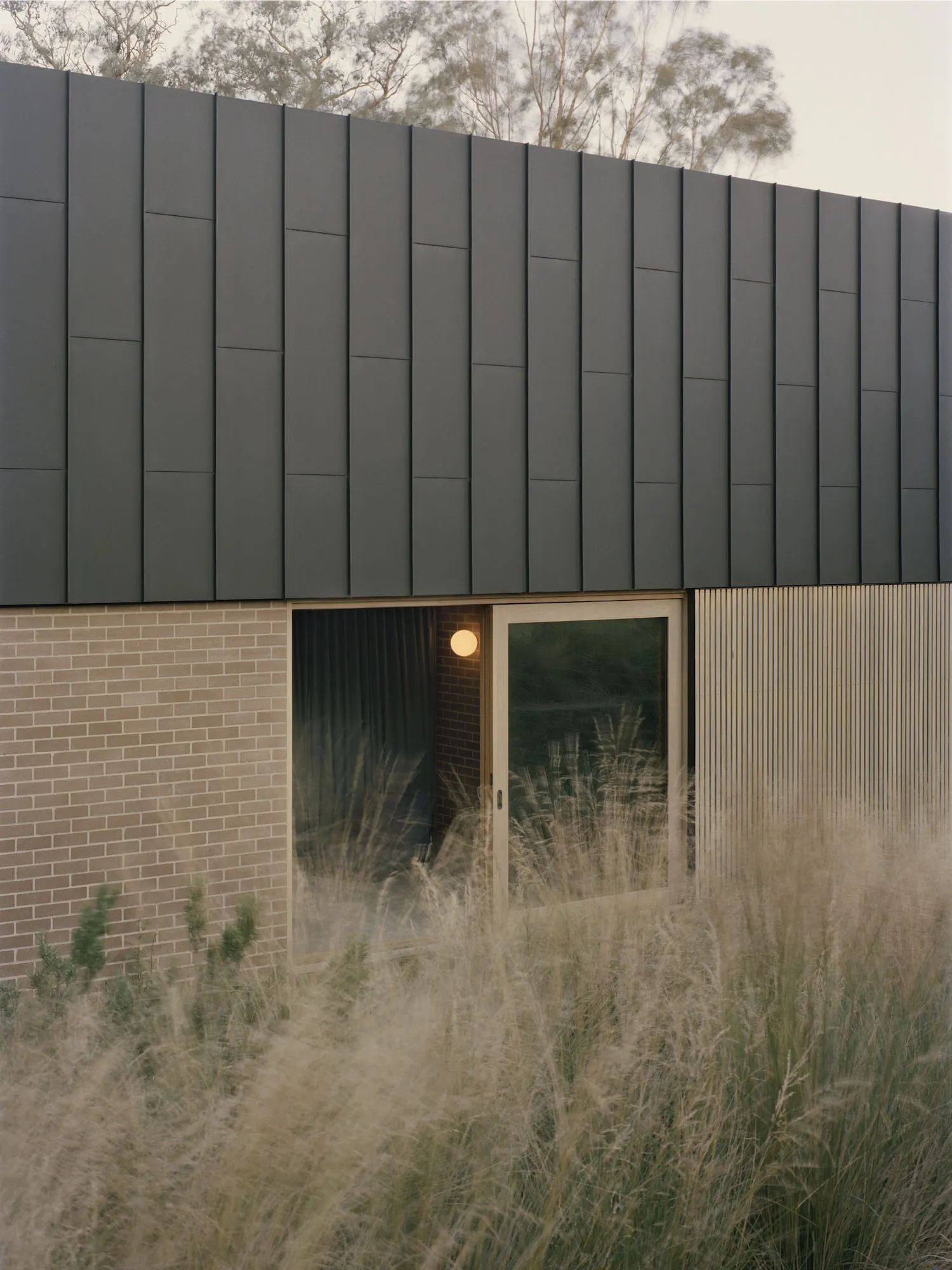 Exterior view of a house with a black roof, brick wall, and natural light from windows