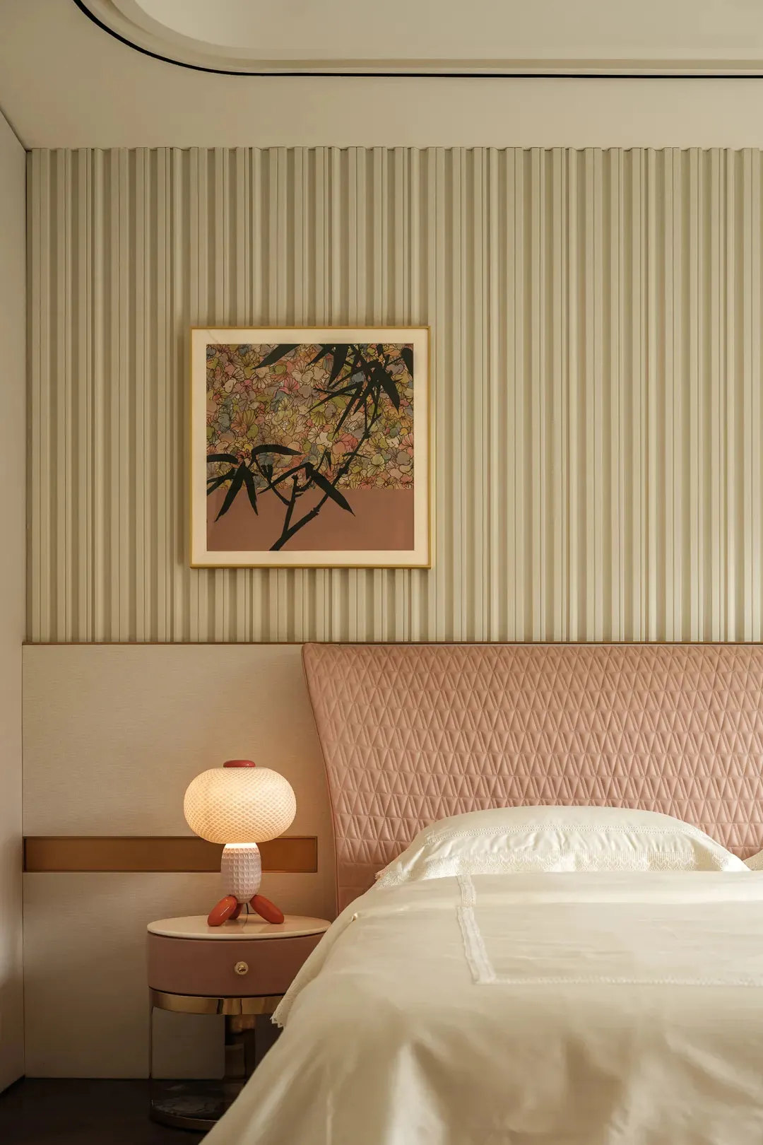 A cozy bedroom with a large bed, white bedding, and a painting of flowers on the wall, lit by two lamps and a vase