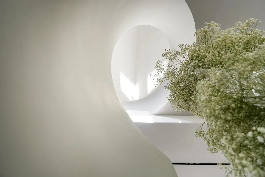 A calm indoor space with a white wall, a large vase with purple flowers, and a serene atmosphere