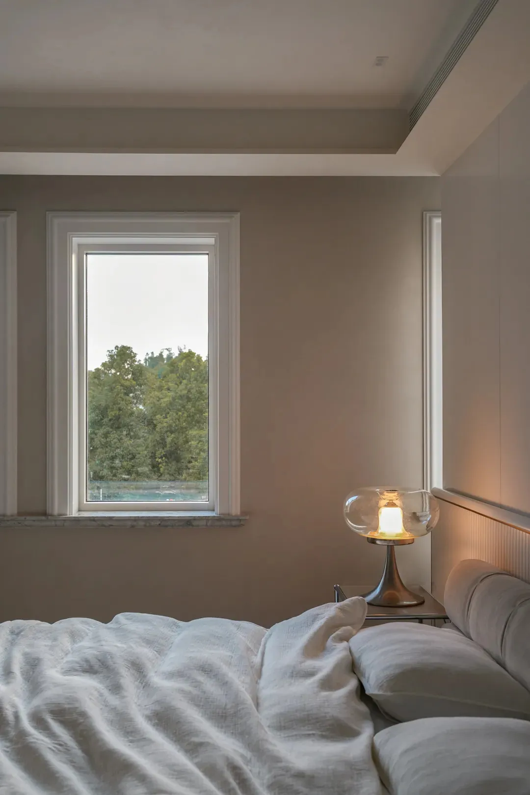 A bedroom with a large window, a neatly made bed, and two nightstands, creating a calm and inviting atmosphere