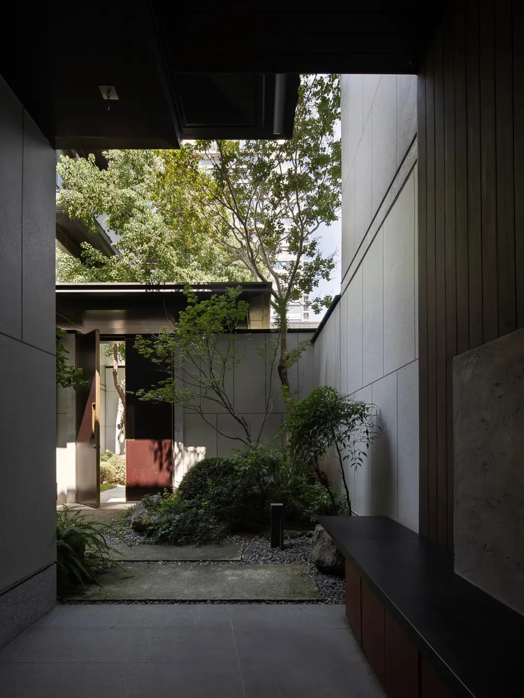 A serene courtyard scene with a tree, two benches, and a mix of architectural elements and natural surroundings