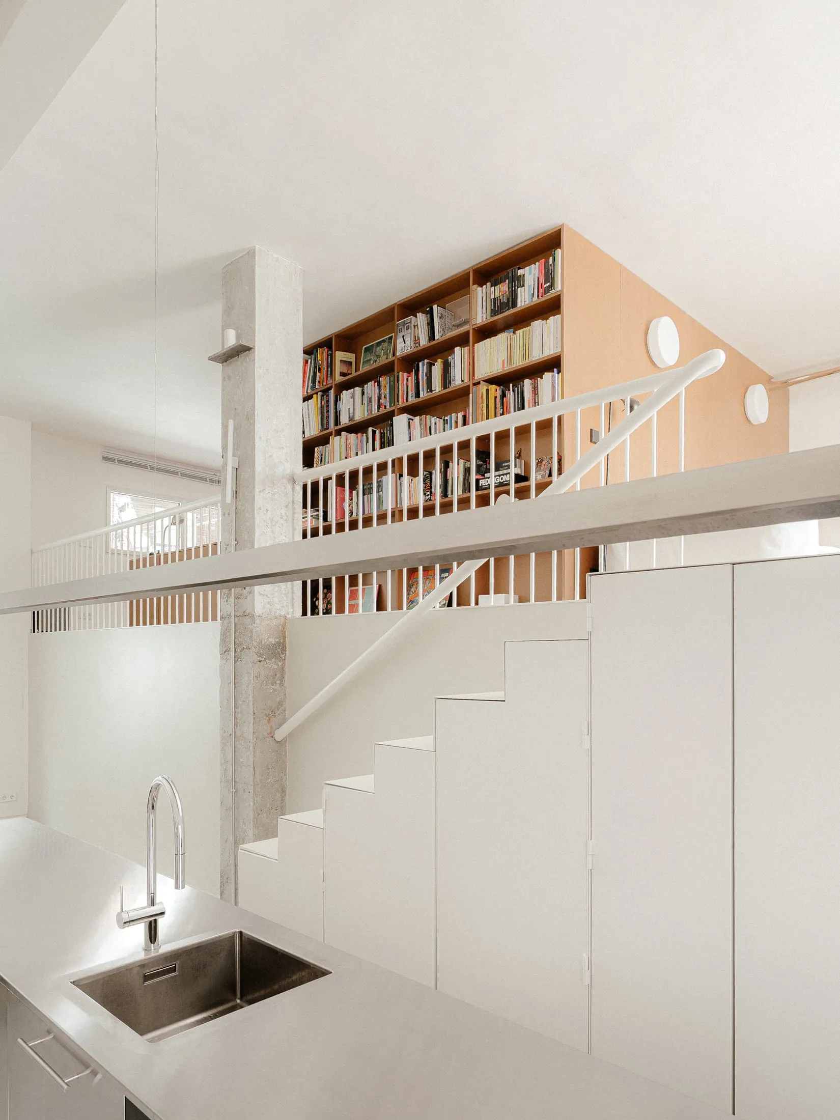Open living area with a kitchen, wooden stairs, white cabinets, and scattered books creating a warm and inviting atmosphere