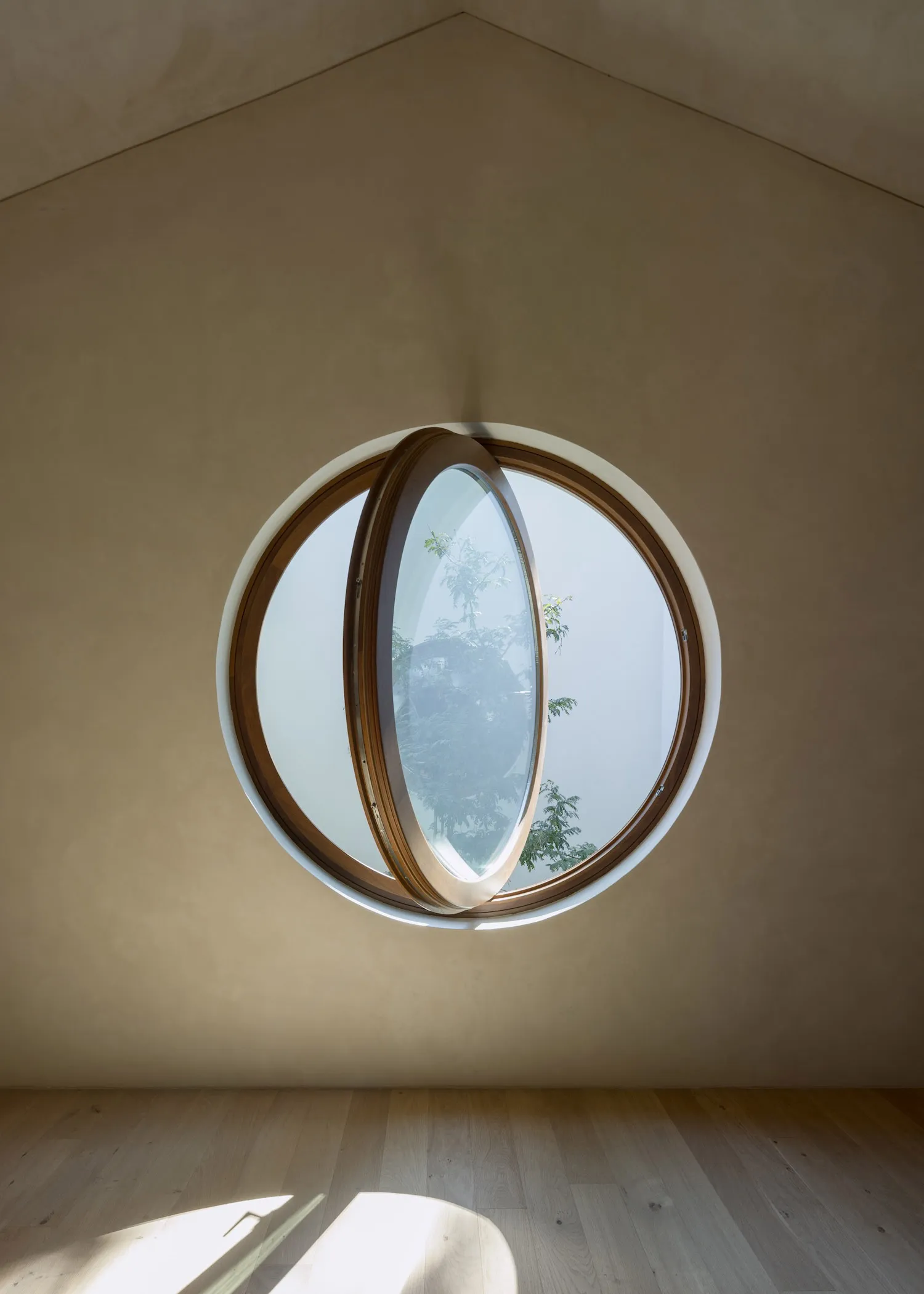 A modern room with a round window made of wood and glass, surrounded by white walls and wooden elements