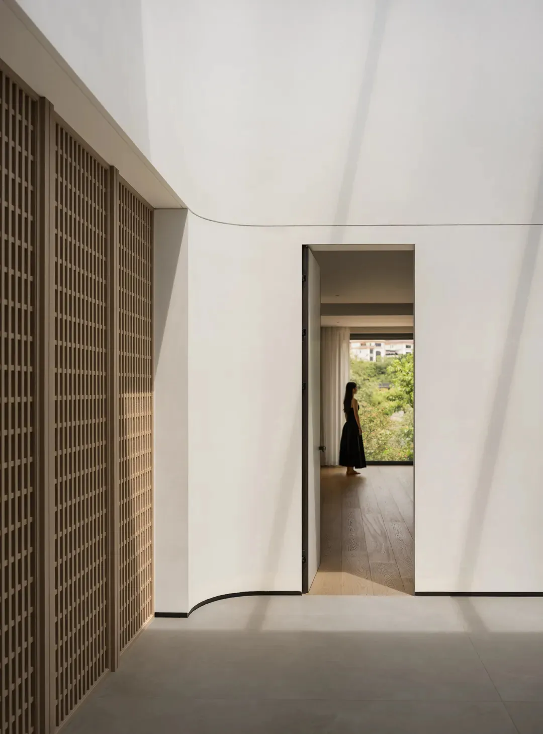 A woman stands near a doorway in a calm and peaceful hallway made of wood with a natural ambiance