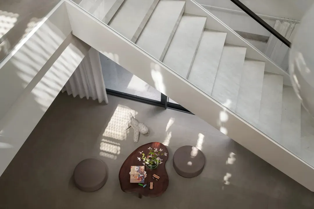 Bright open living area with a white staircase, two couches, a dining table, and a potted plant, surrounded by ample seating options