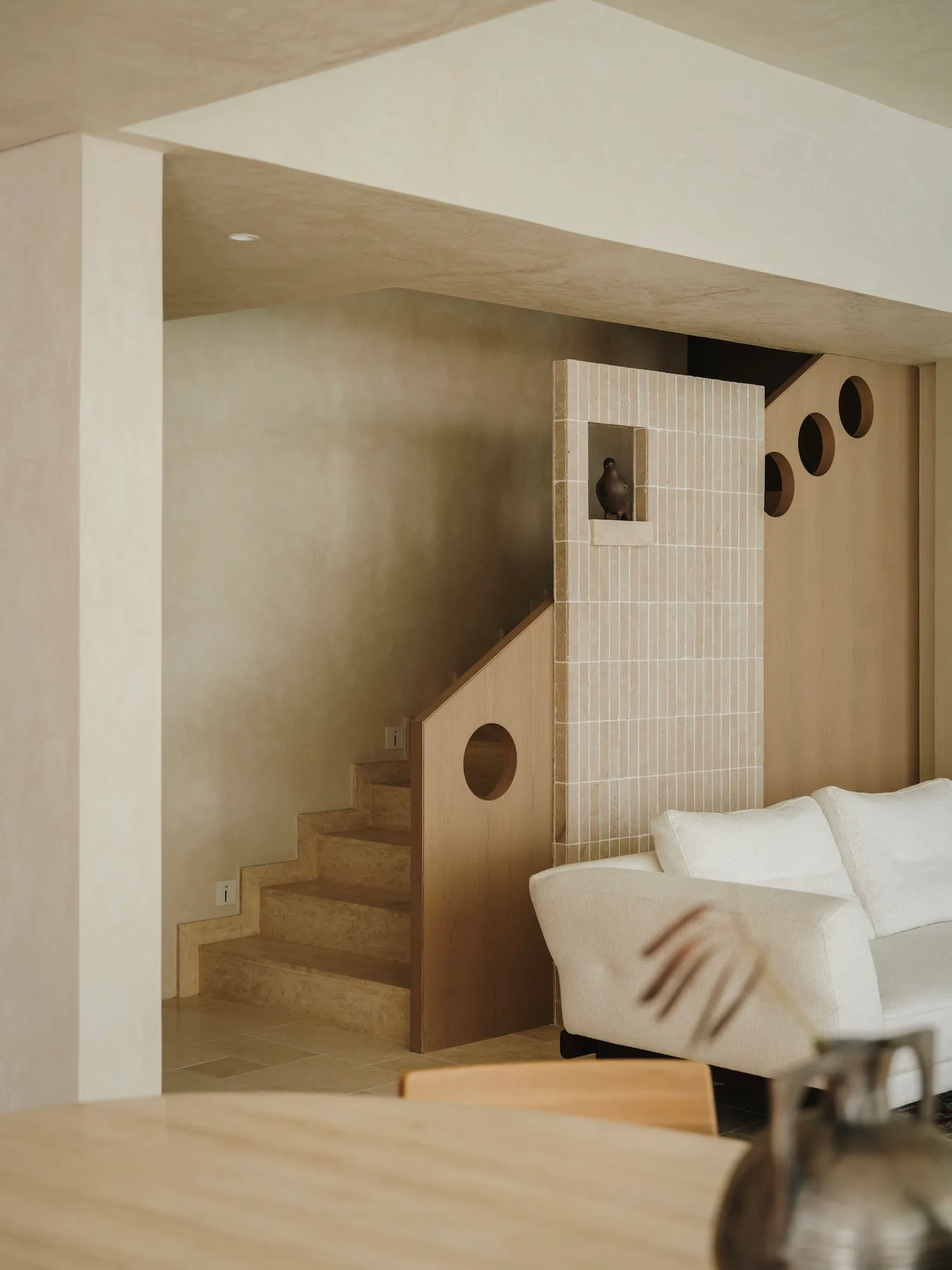 Cozy living space with a white couch, wooden staircase, and a chair, inviting atmosphere