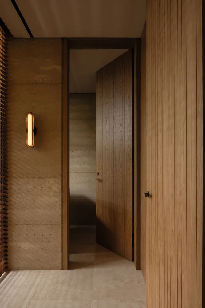 A warm and inviting hallway with wooden features, lit by a single light source, revealing a room beyond two open doors