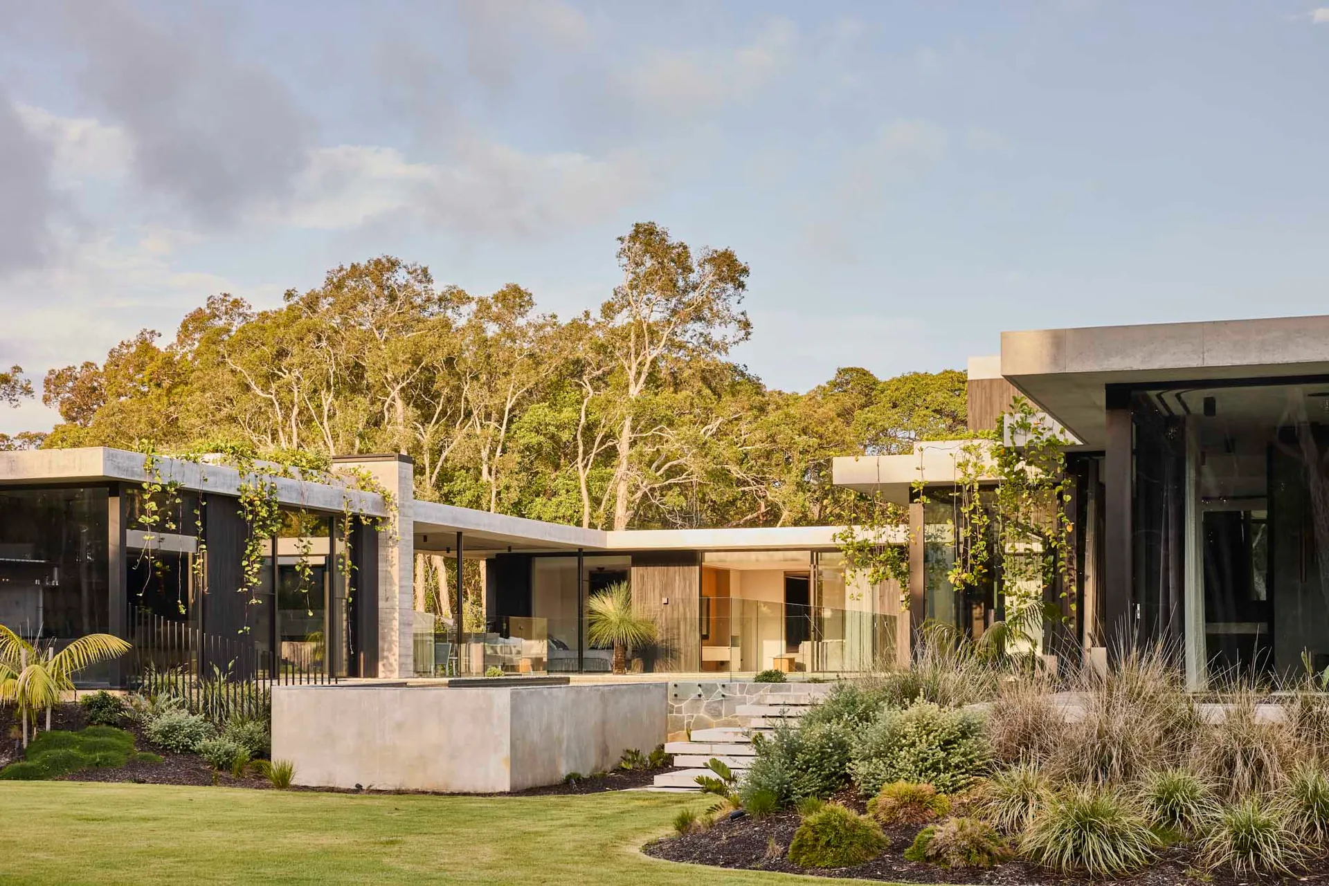 A modern house with a large glass wall facade, surrounded by two potted plants and three outdoor chairs, set in a contemporary and stylish living environment
