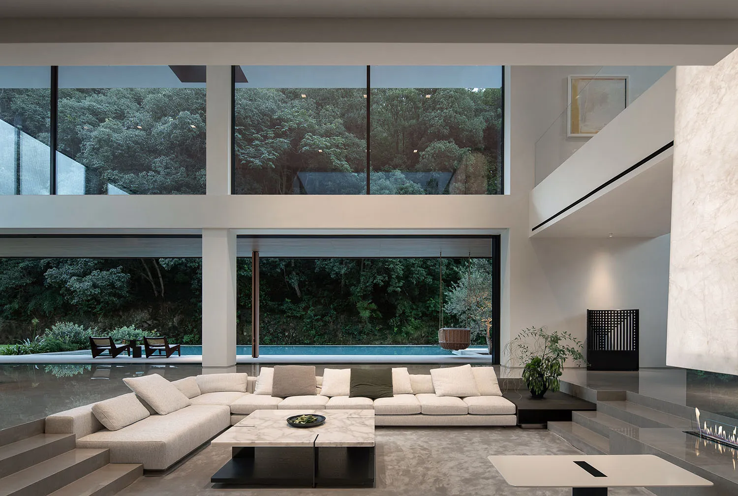 Open modern living area with a white couch, glass wall, chairs, and dining table, giving off a clean and minimalist vibe