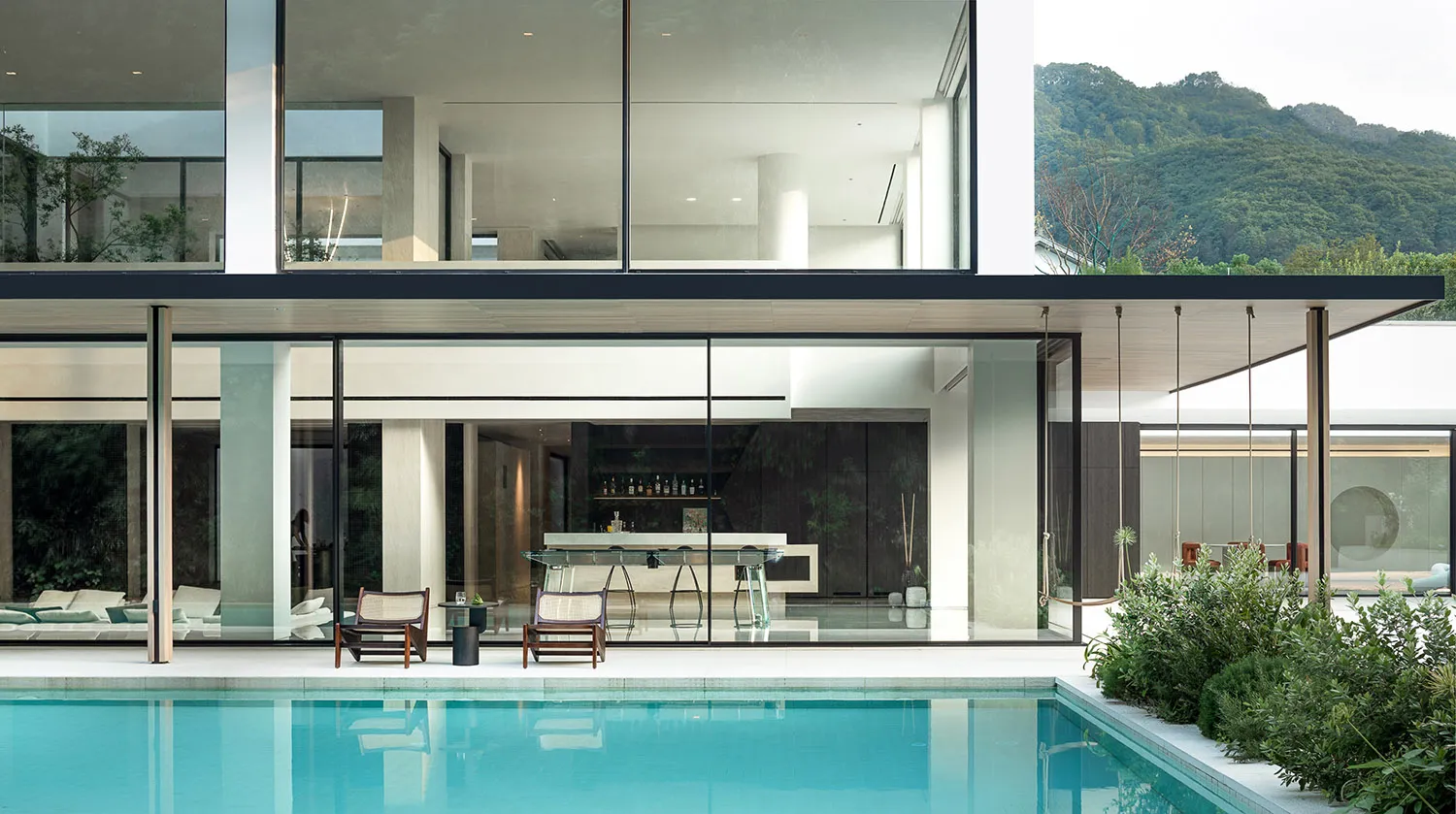 A relaxing pool area with natural light pouring in through large windows, surrounded by chairs and decorative bottles