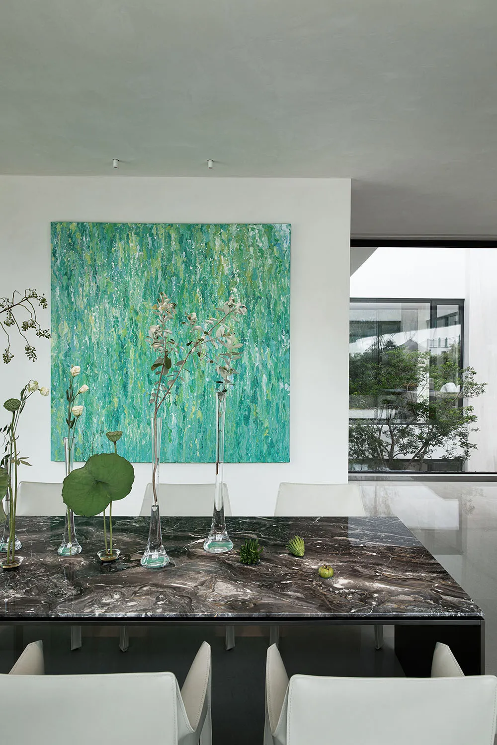 A cozy dining space with a table, chairs, vases with flowers, potted plants, and a painting on the wall
