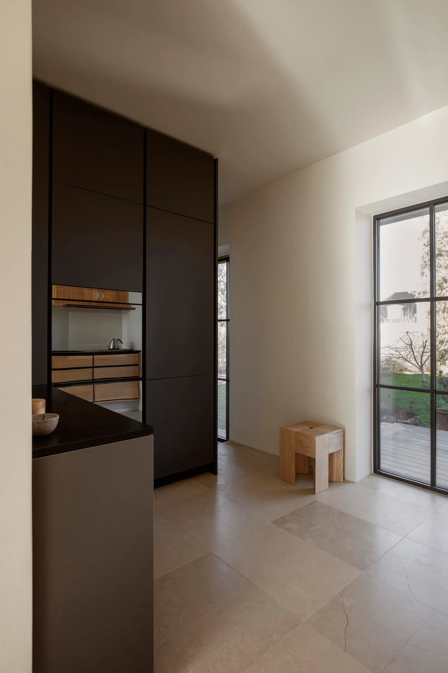 Empty kitchen with black cabinets, white walls, and two windows, well-lit and minimalist