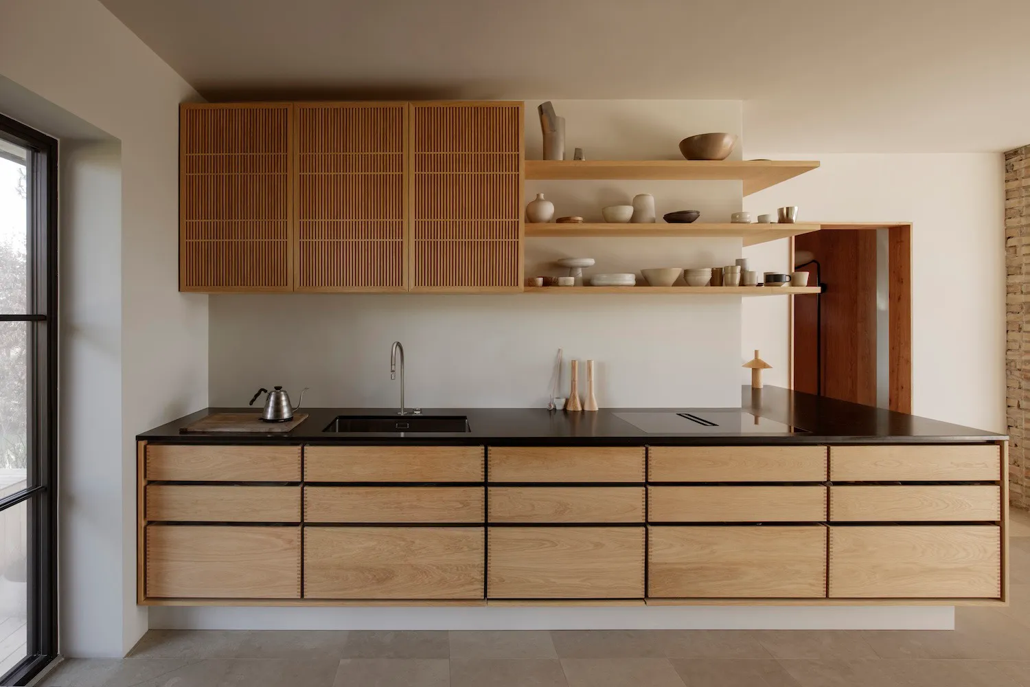 A modern kitchen with wooden cabinets, black countertops, a sink, dining table, and various kitchenware