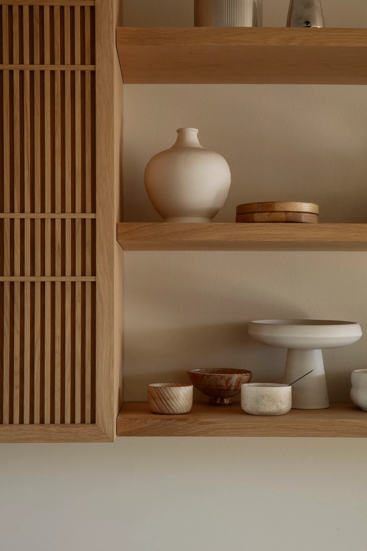 A wooden bookshelf with bowls, vases, and cups arranged on its shelves, showcasing a functional storage solution