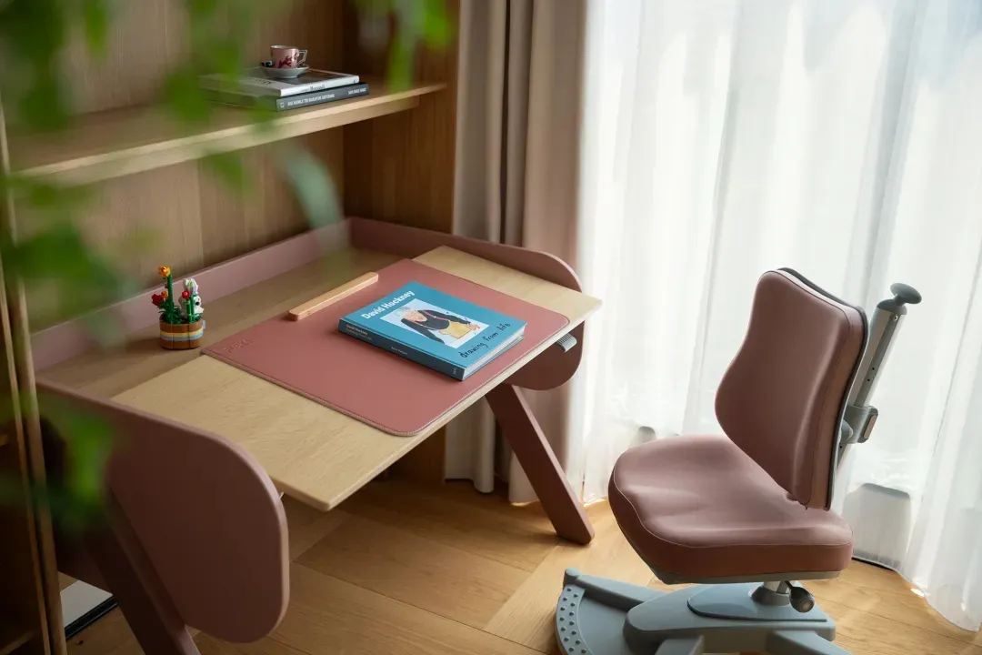 A calm and organized office space with a pink desk, two chairs, and a book, set against a neutral-toned background