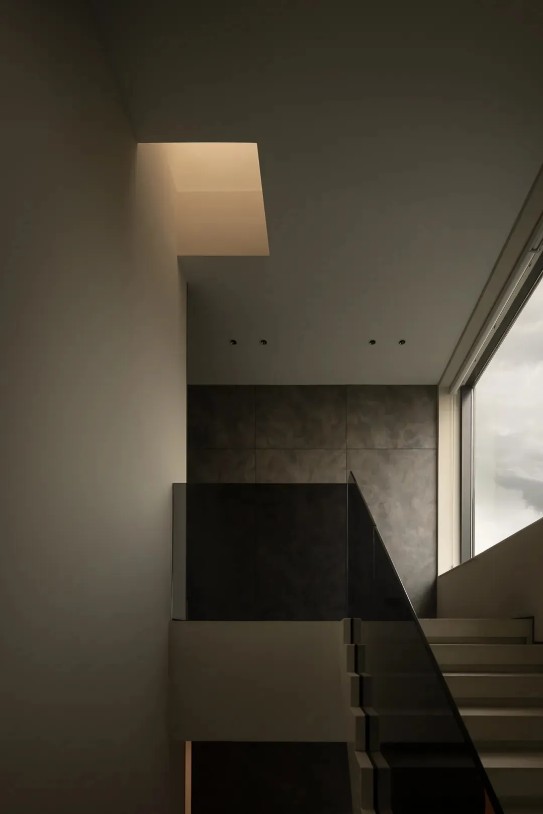 A dimly lit staircase with concrete steps and a window above, casting natural light into the space