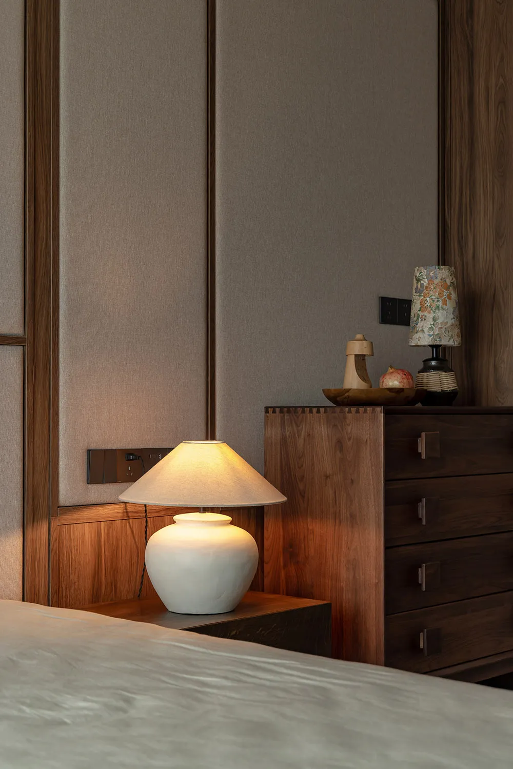 Cozy bedroom with wooden walls, a dresser, two lamps, and a vase, creating a warm and inviting atmosphere