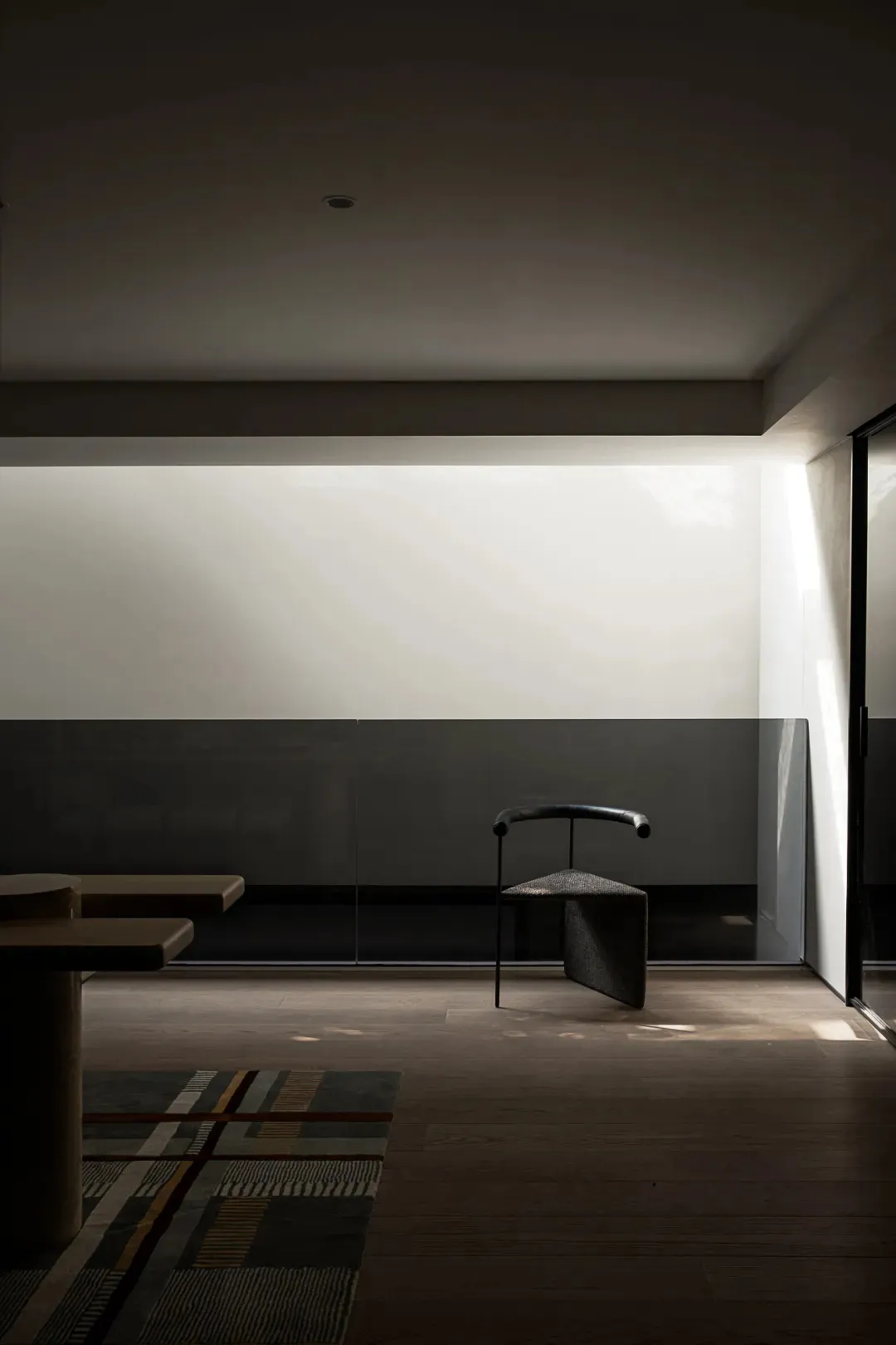 Empty modern room with a black chair in front of a glass wall, surrounded by white walls and a minimalist aesthetic