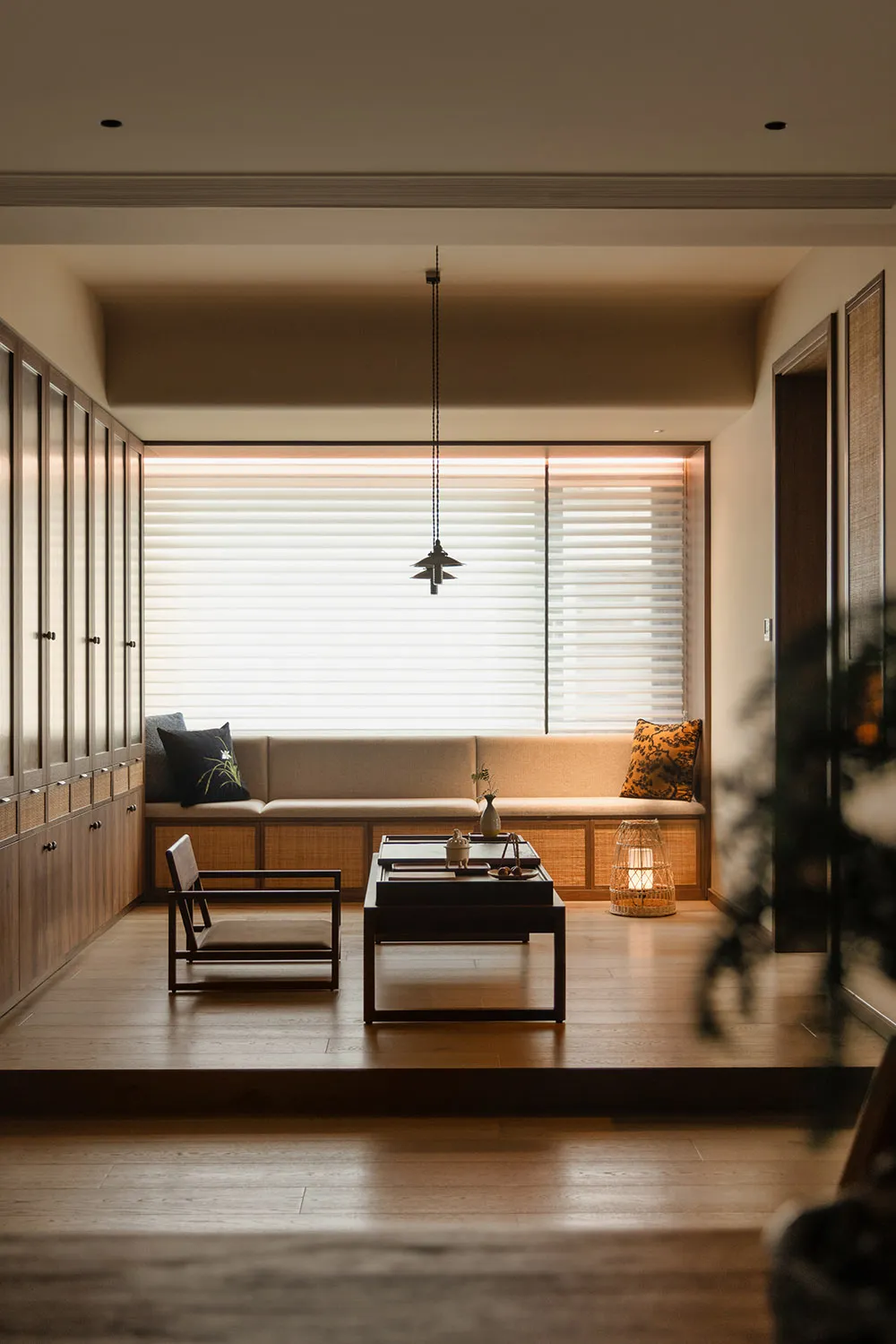 Well-lit living area with a couch, chair, dining table, and potted plants, decorated in neutral tones with a wooden floor
