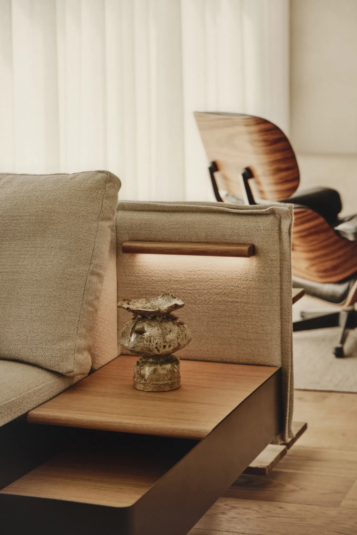 A modern living room with a couch, chair, and ottoman, featuring a wooden backrest and a small table, designed for comfort and conversation