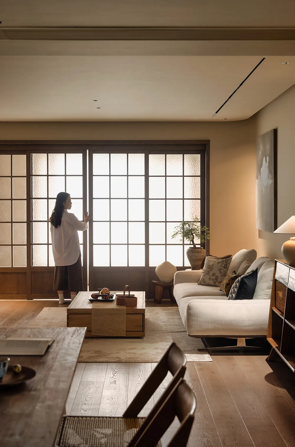 Cozy living space with a white couch, chairs, dining table, and a potted plant, lit by natural light through open doors