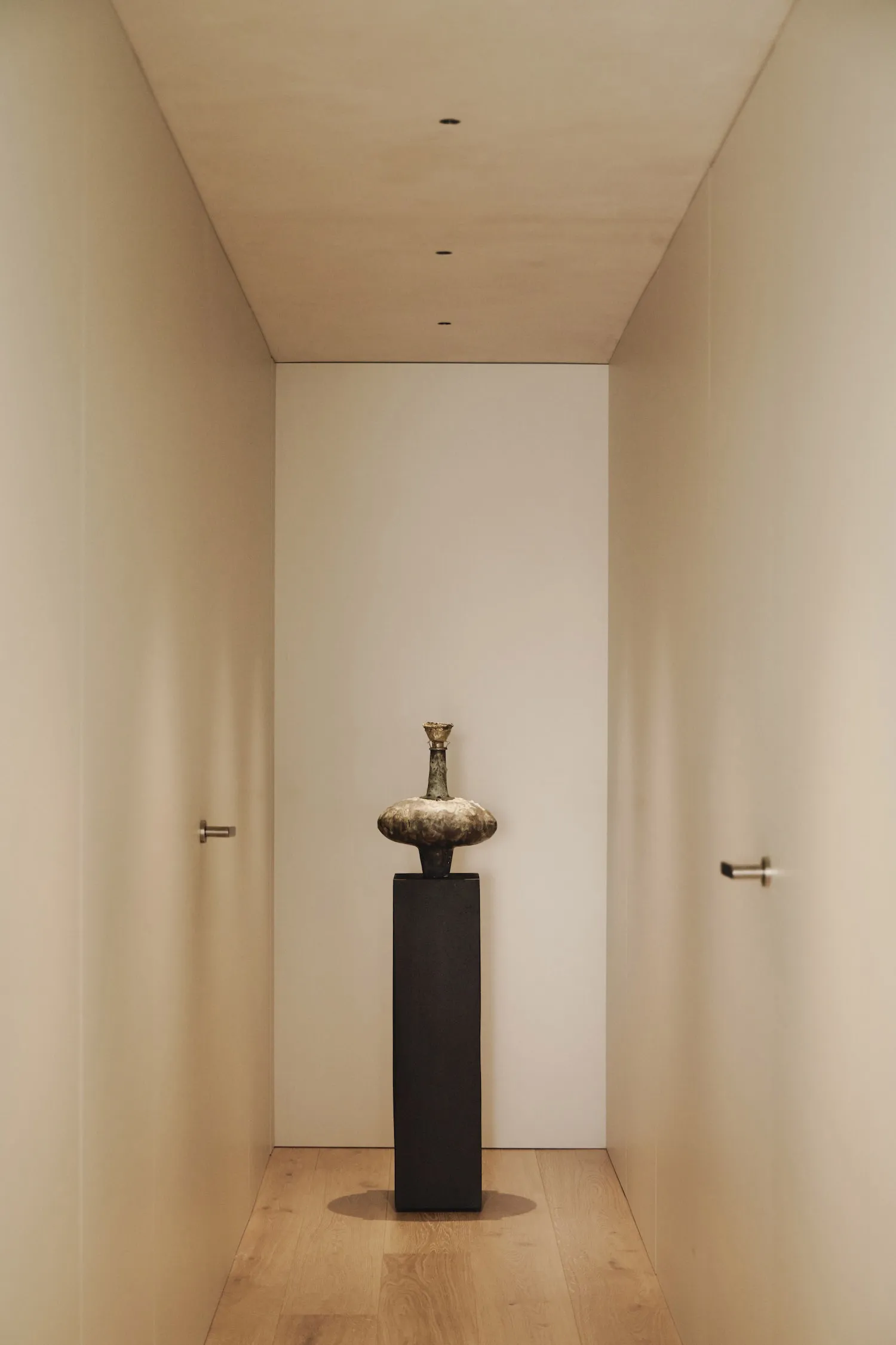 Empty hallway with white walls, a black metal vase on a pedestal, and a minimalist aesthetic