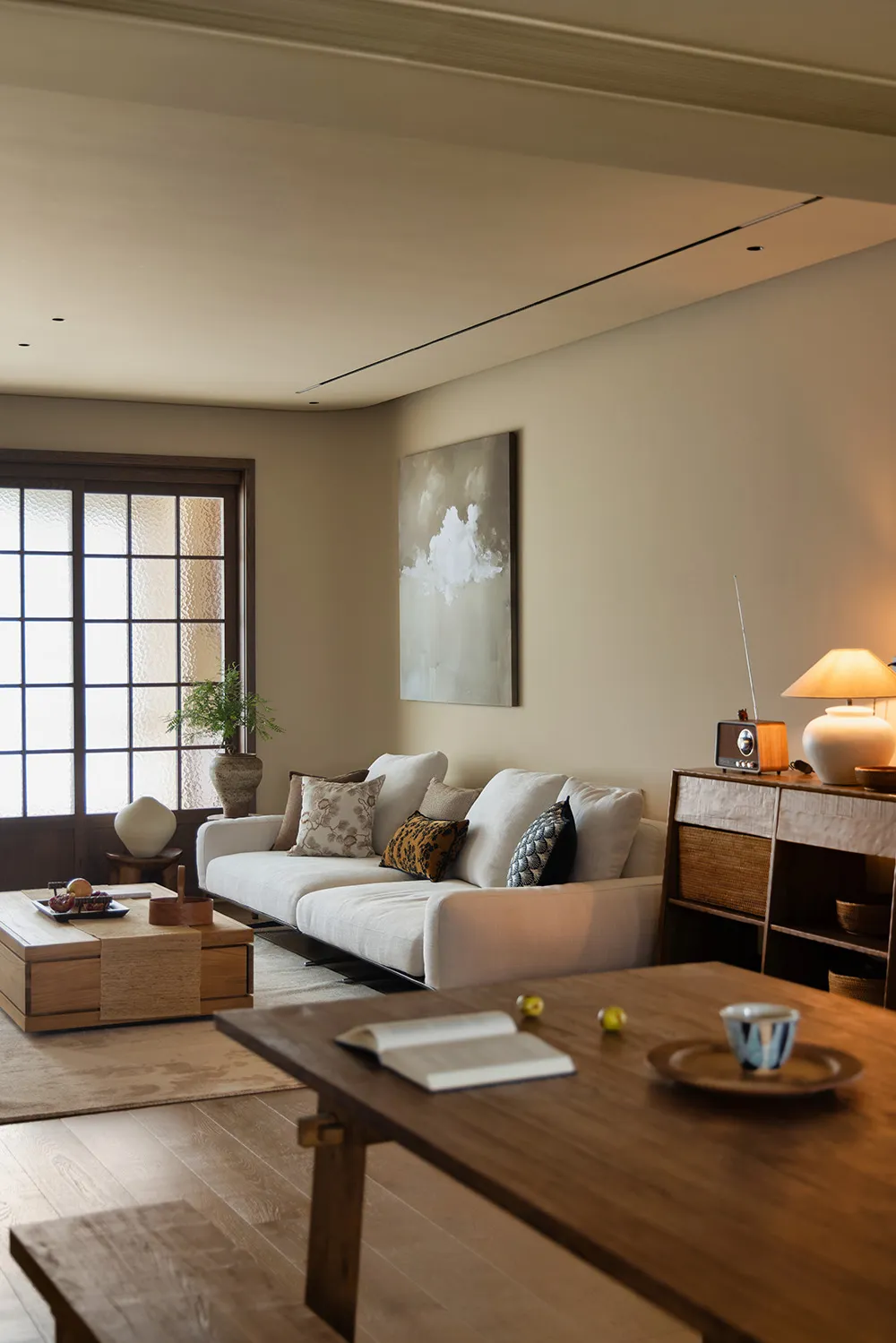 Cozy living room with a white couch, chairs, potted plants, vases, bowls, cups, books, and a remote control, creating a warm and inviting atmosphere