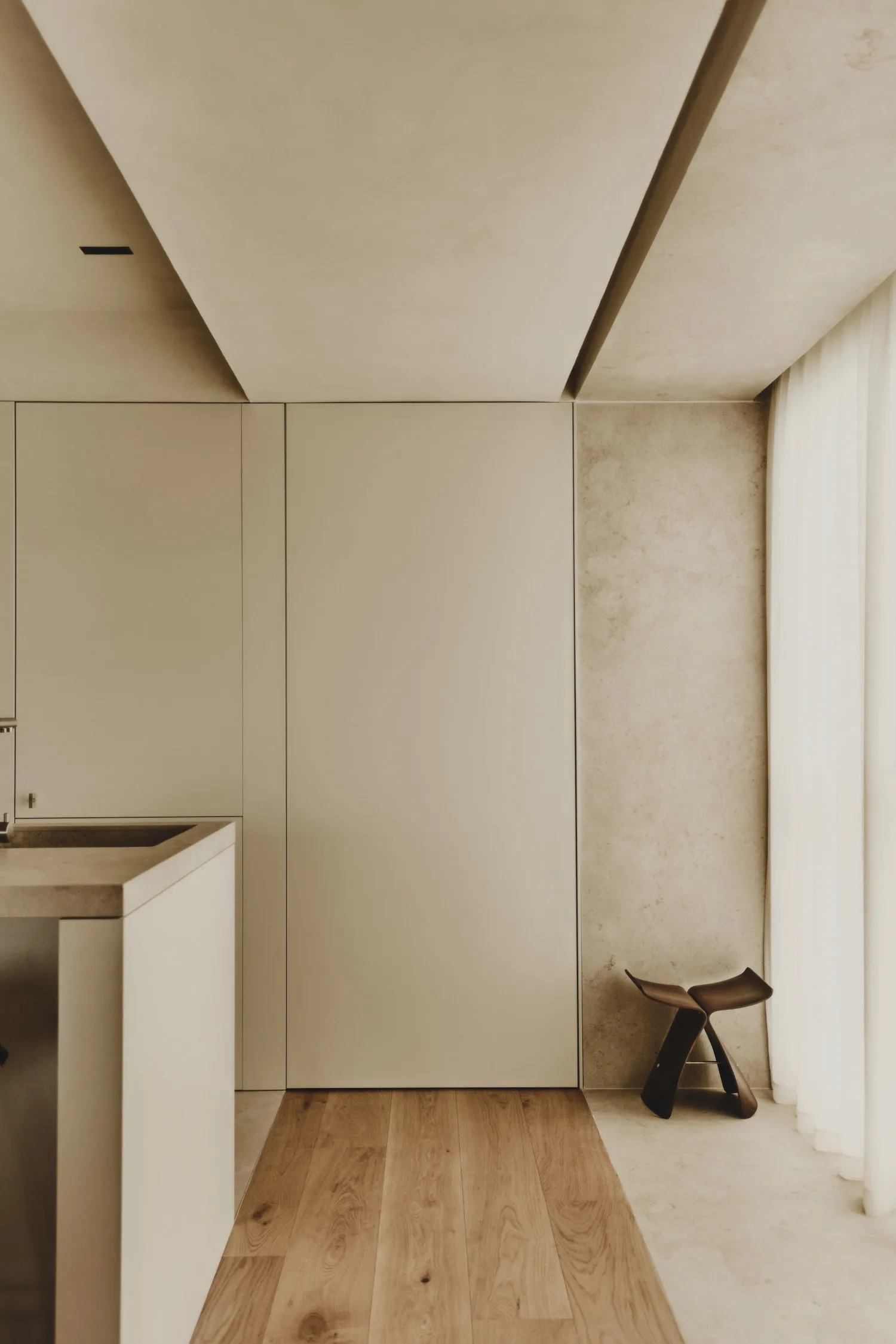 Empty modern kitchen with white cabinets, a sink, and a chair, set against a concrete wall background