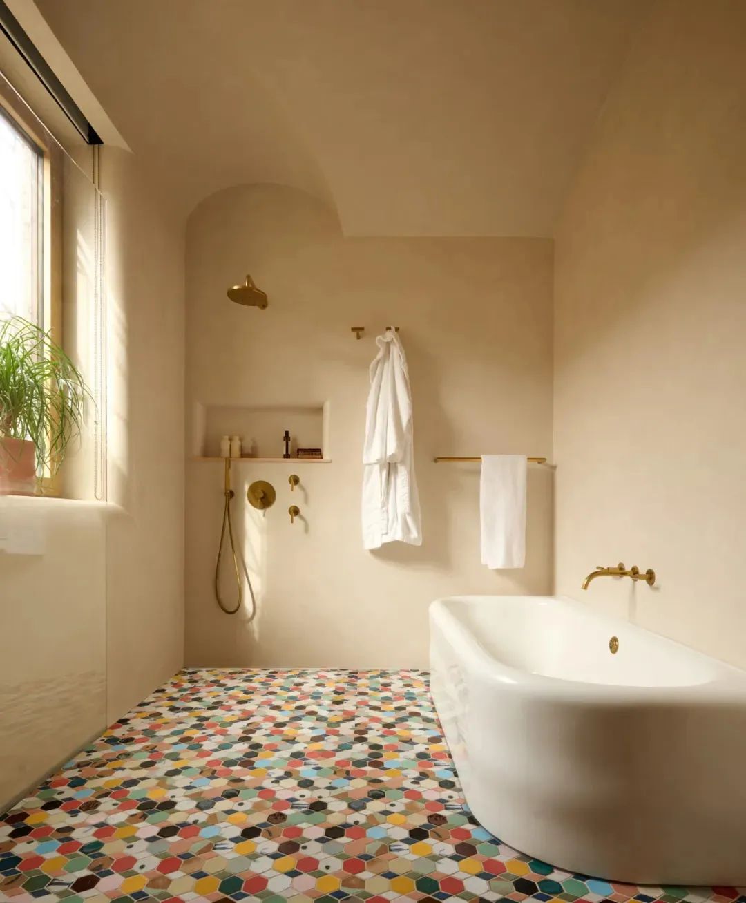 A bathroom with a white bathtub under a window, featuring gold fixtures, two bottles, and three potted plants creating a calming atmosphere