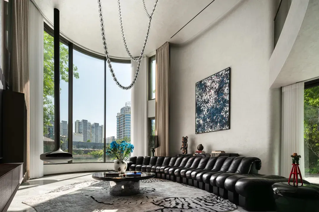 Elegant living room with black leather couches and chairs, natural light, and decorative vases, with books scattered on surfaces