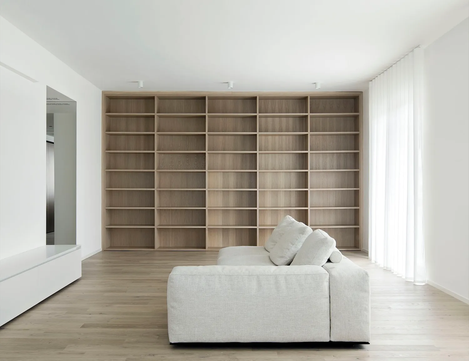 Empty modern living room with wooden floors and white walls, featuring two couches and a chair in an open concept space