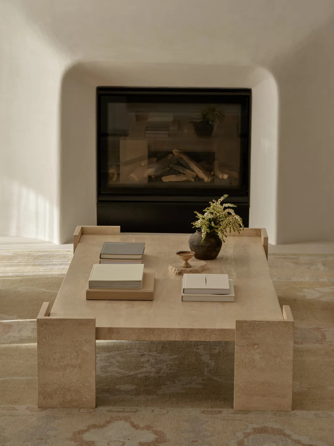 Cozy living area with a fireplace, table, and books, well-lit by natural sunlight