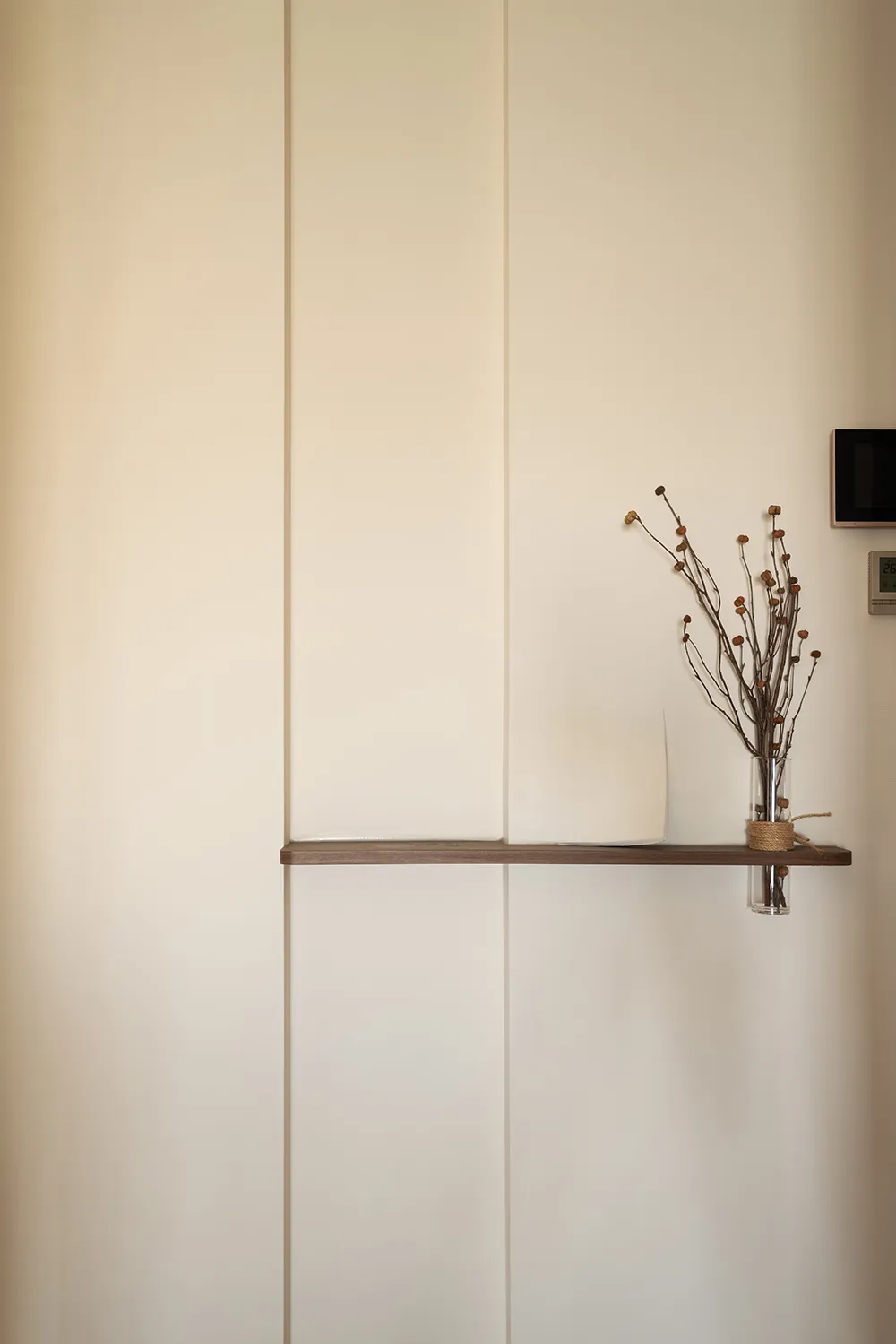 A calm interior space with a white wall, wooden shelf, and vases with flowers, creating a peaceful atmosphere