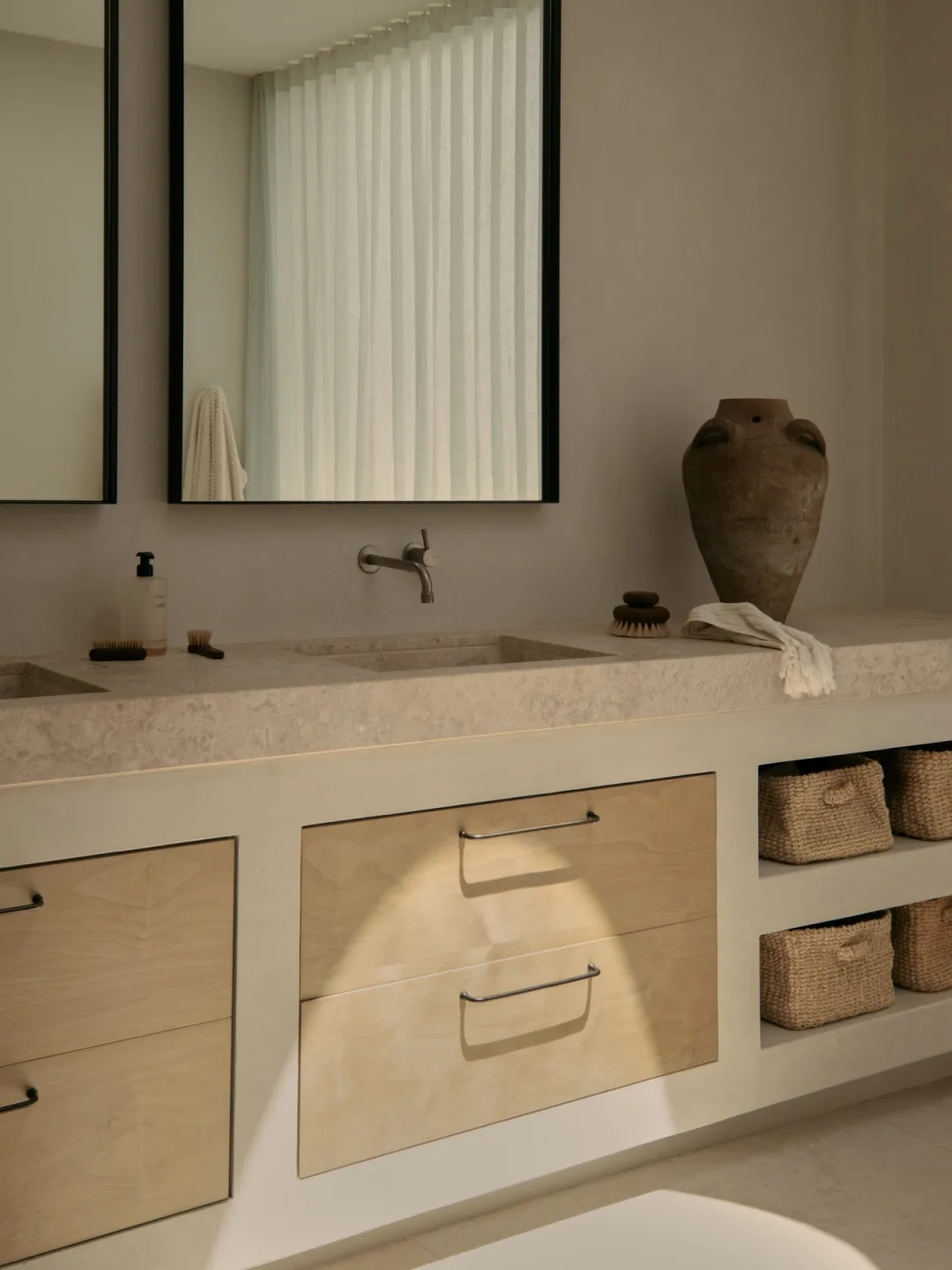 A modern bathroom with a white theme and wooden elements, featuring a sink, mirror, and storage cabinet, with two bottles on the countertop and bright inviting lighting