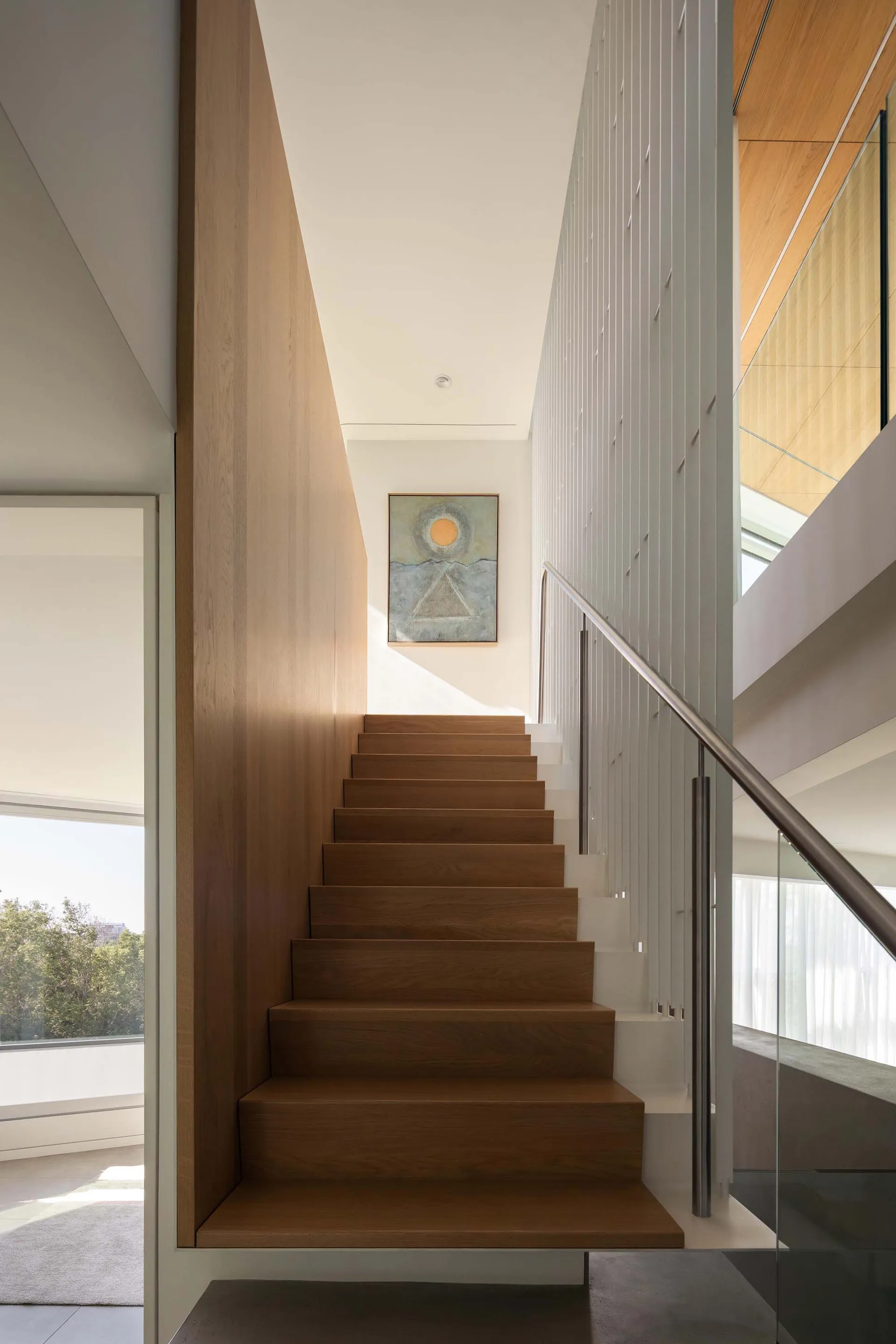 Warm and inviting interior space with a wooden staircase, a painting above, and natural light