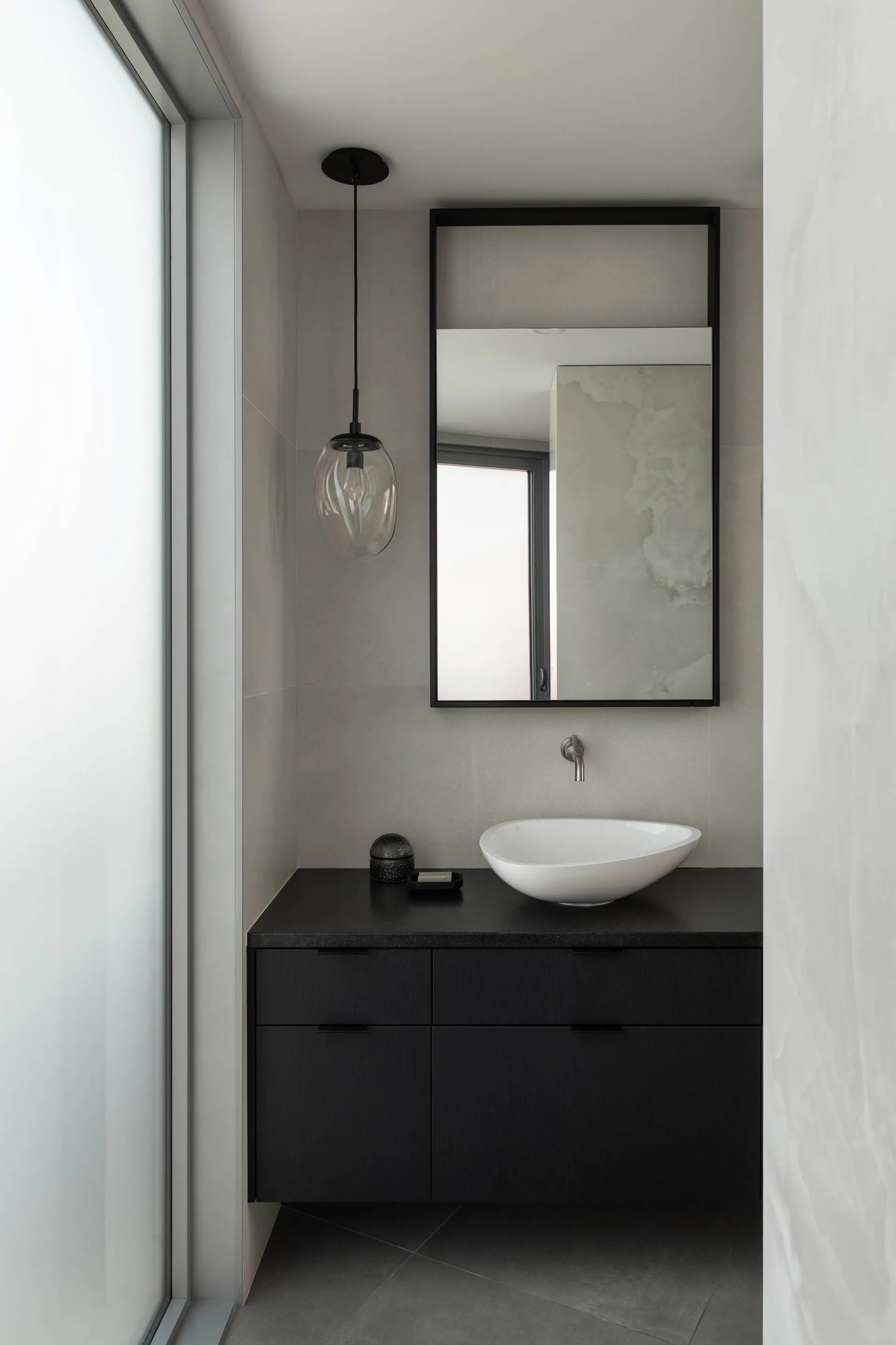 A small bathroom with a white sink, mirror, and window, featuring two bottles on the countertop and a clean, organized atmosphere