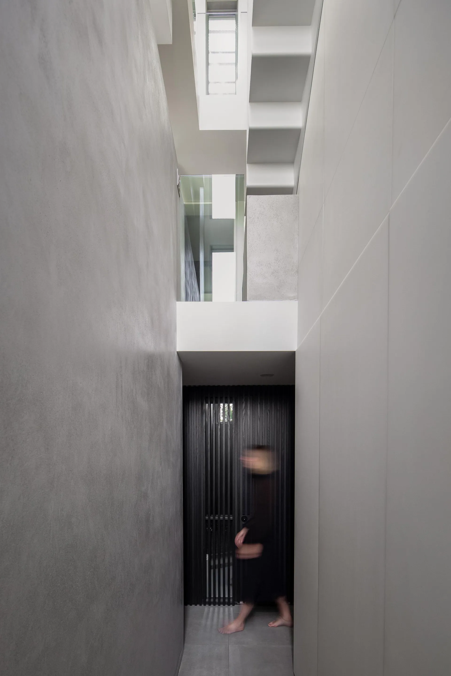 A person walks down a narrow hotel hallway with dark walls and two doors on either side