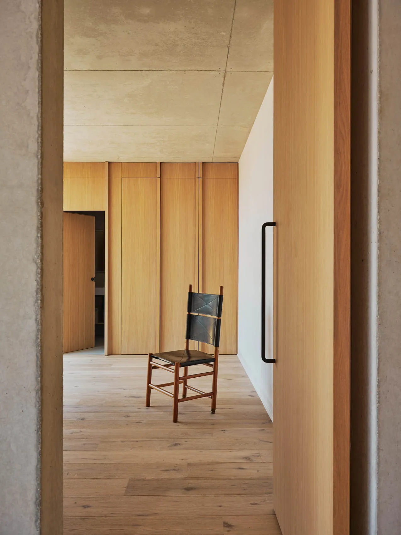 A cozy living area with a wooden floor and a concrete wall, featuring a chair and a backpack, set against a neutral background