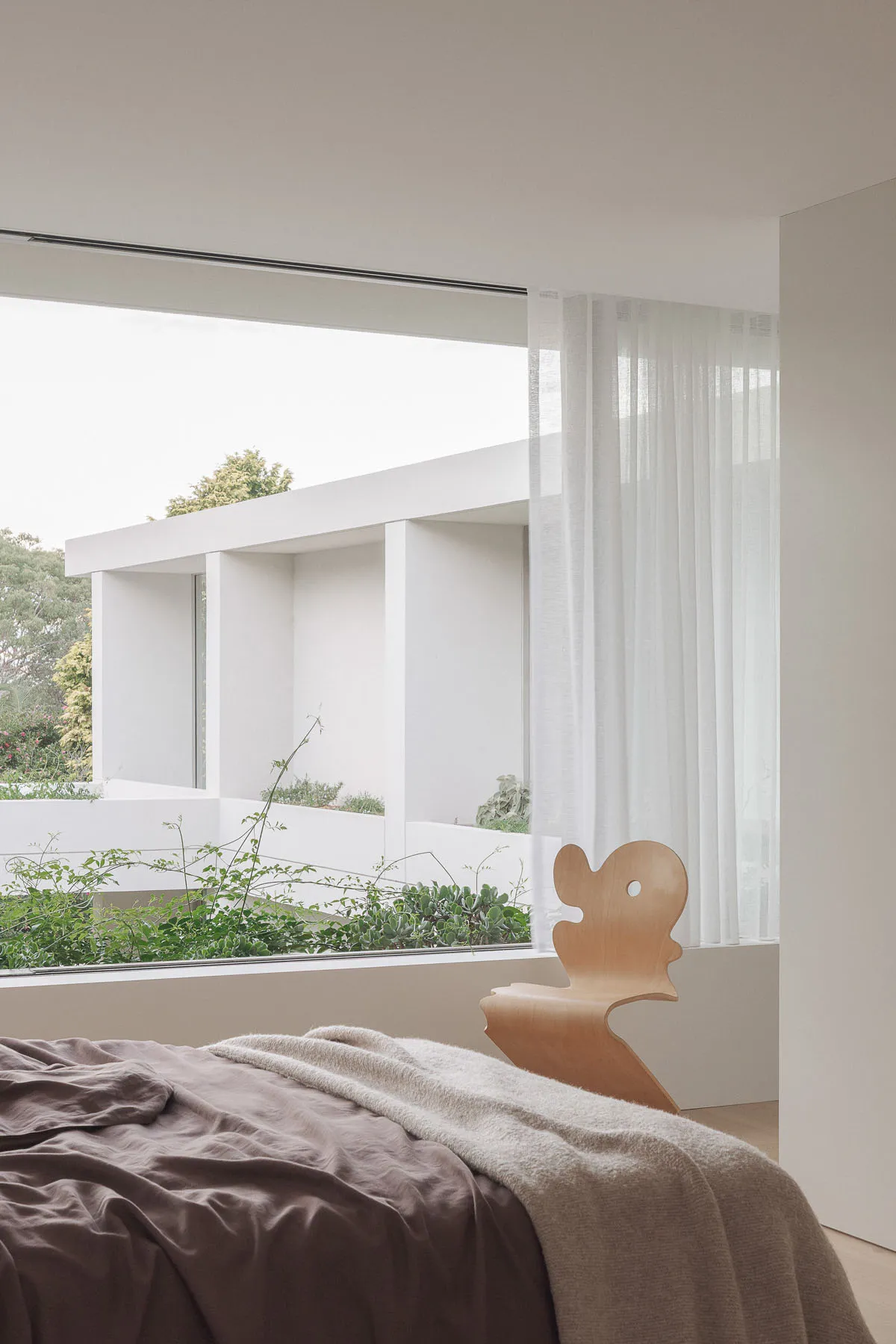 A bright and inviting bedroom with a large window, two chairs, a couch, and greenery outside