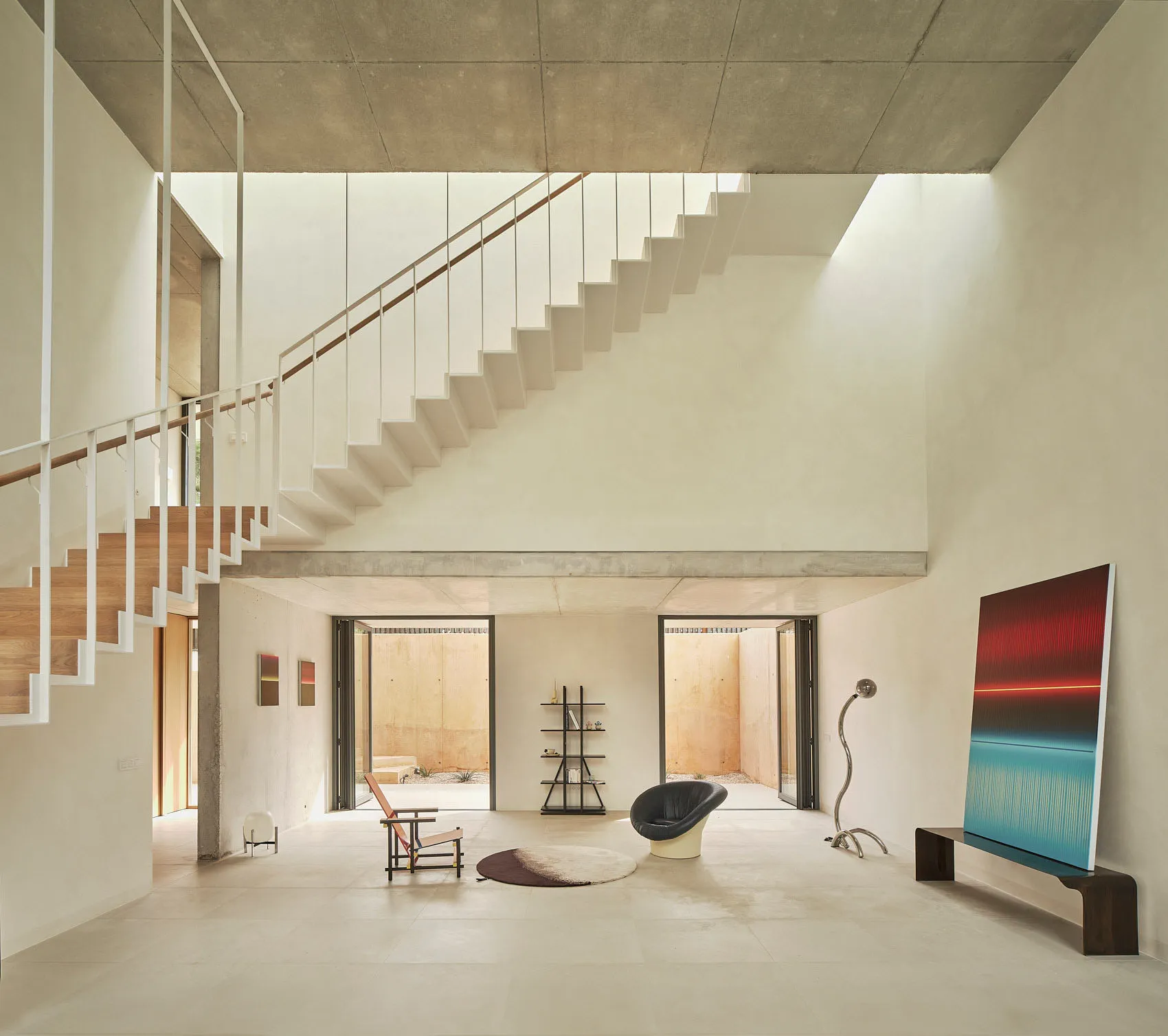 Bright and inviting open living area with a white staircase, minimalist design, two chairs, a couch, and natural light from windows