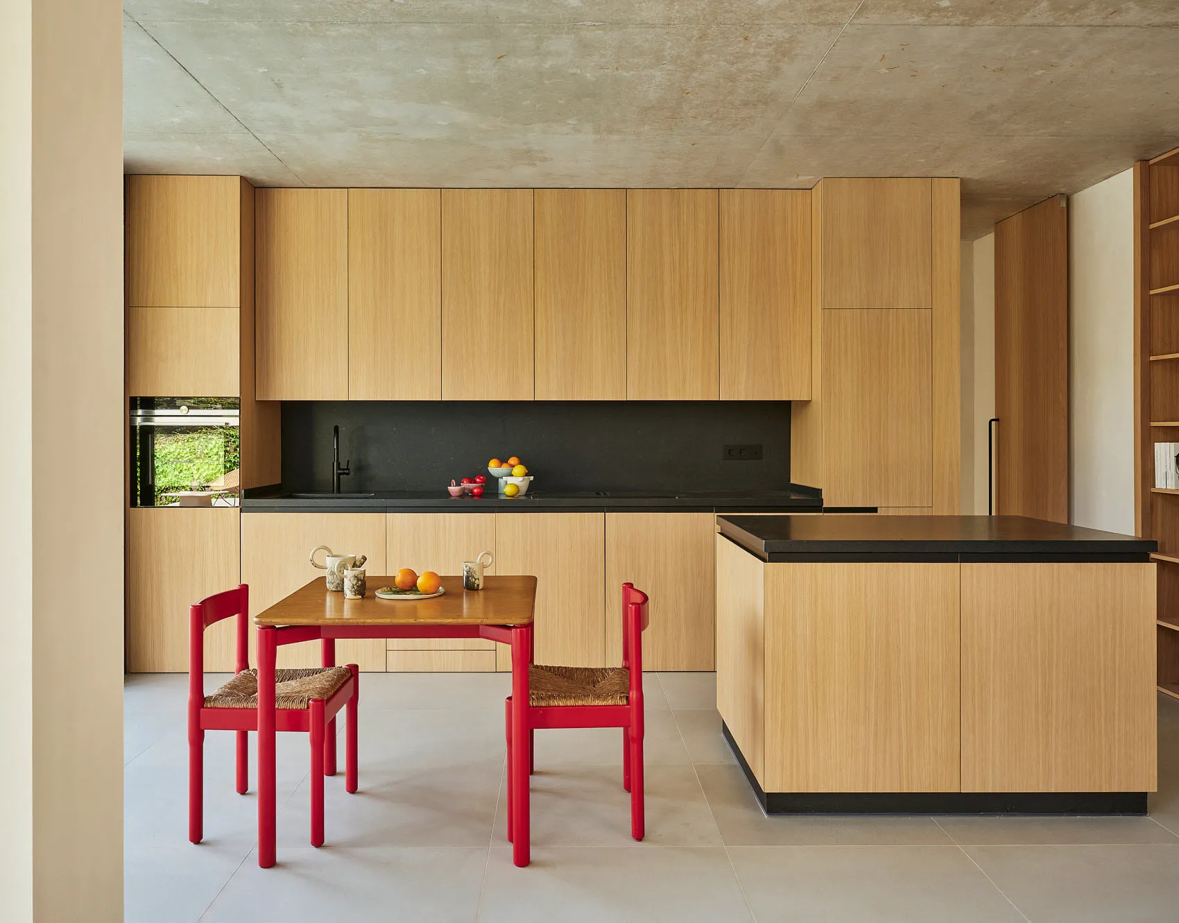 Warm and inviting open kitchen with wooden cabinets and countertops, featuring a few chairs, bottles, cups, bowls, and an orange