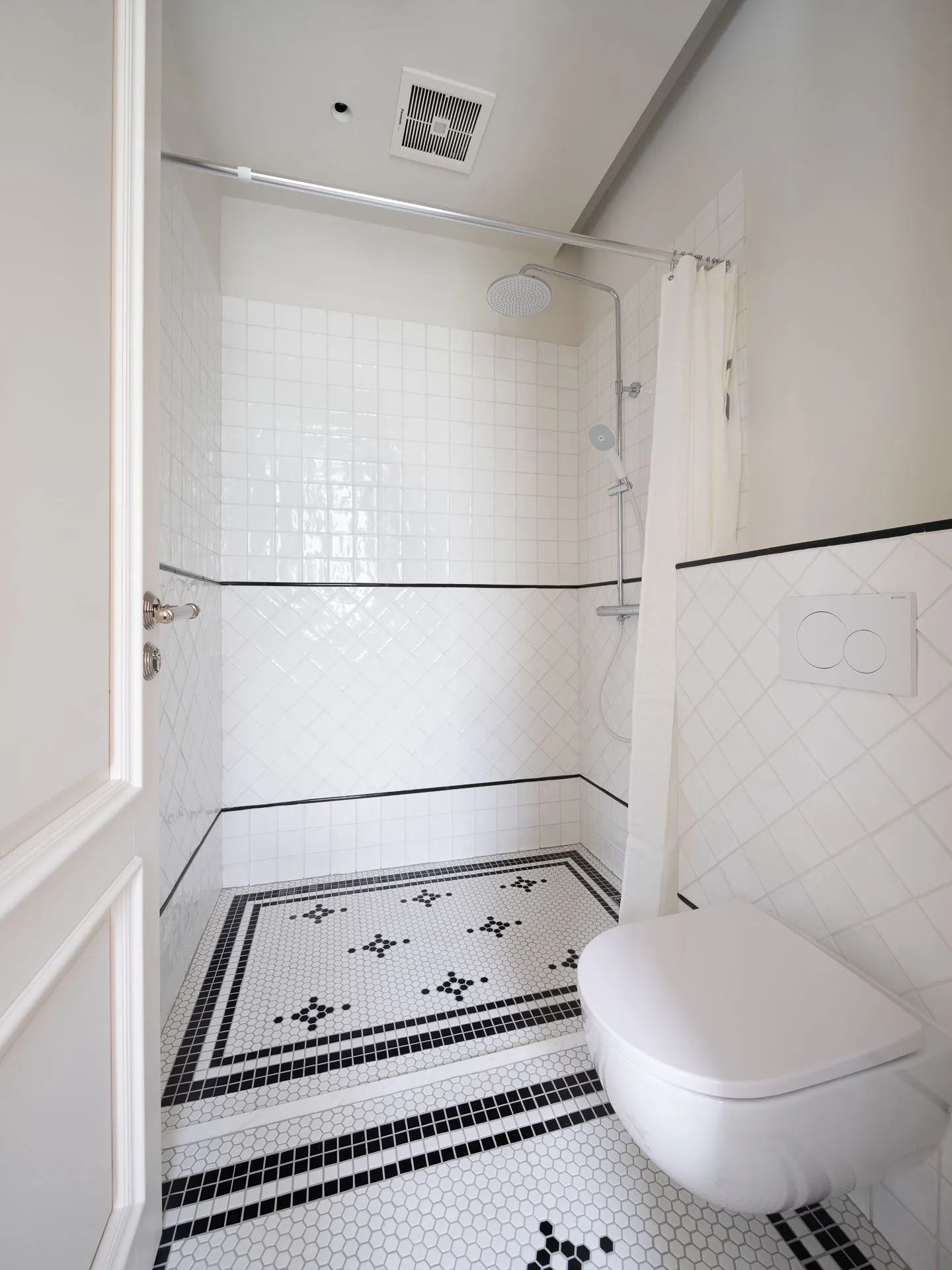 A bathroom with a toilet in the corner, black tile flooring, and two showerheads on either side for easy access