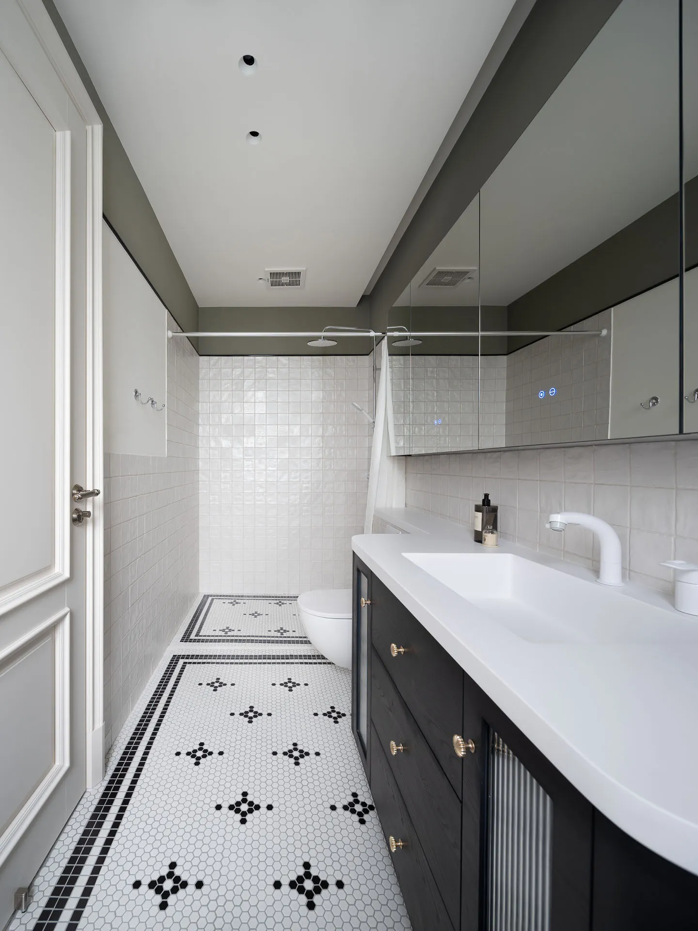 Bathroom with a white sink, toilet, and shower area, surrounded by black and white tiles, a mirror above the sink, and a clean, modern design